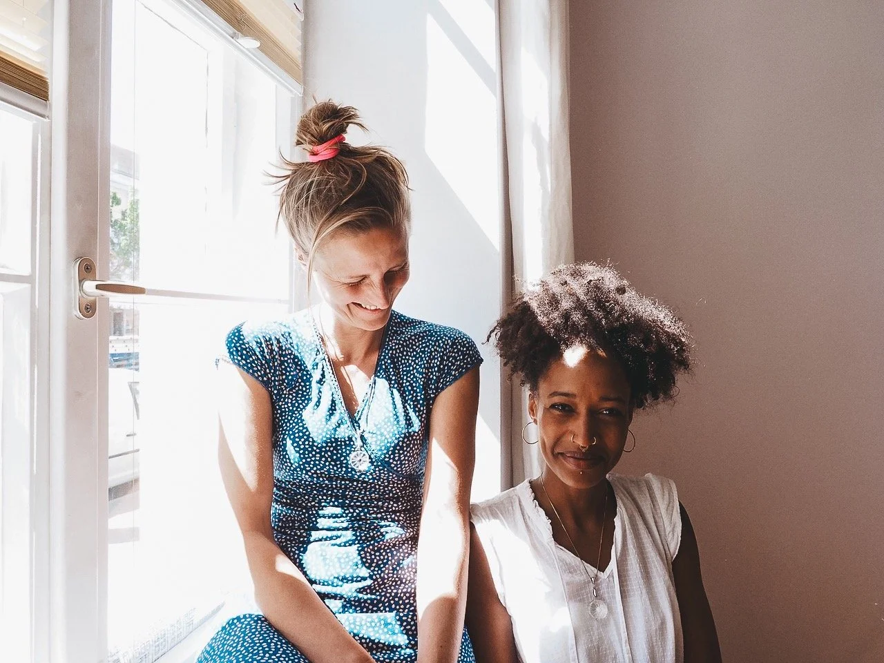 Zwei Frauen sitzen nebeneinander im Sonnenlicht, lachen und haben Spaß.