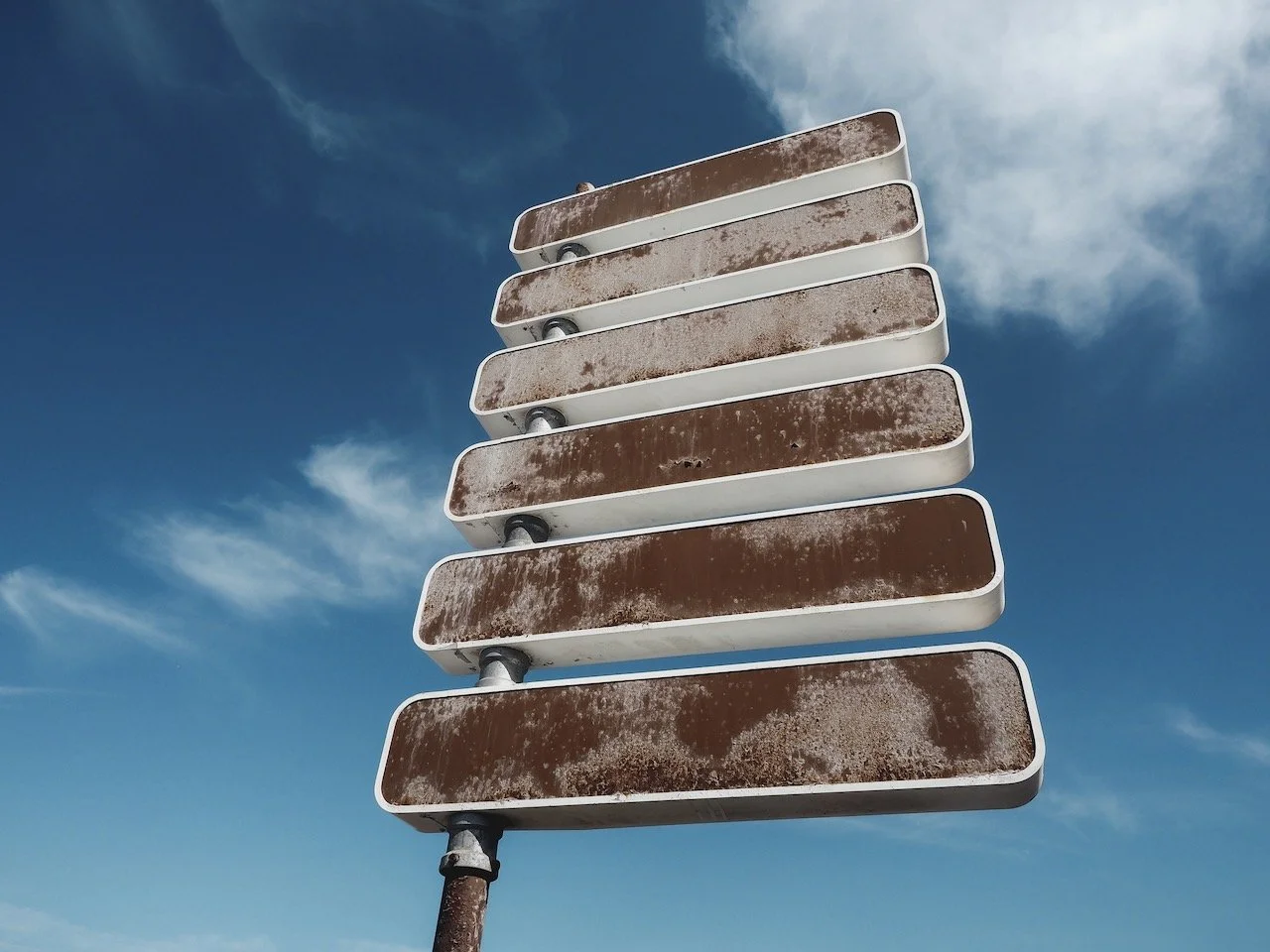 Alter, verrosteter Fahrbahnweiser mit leeren Schildern gegen den Himmel.