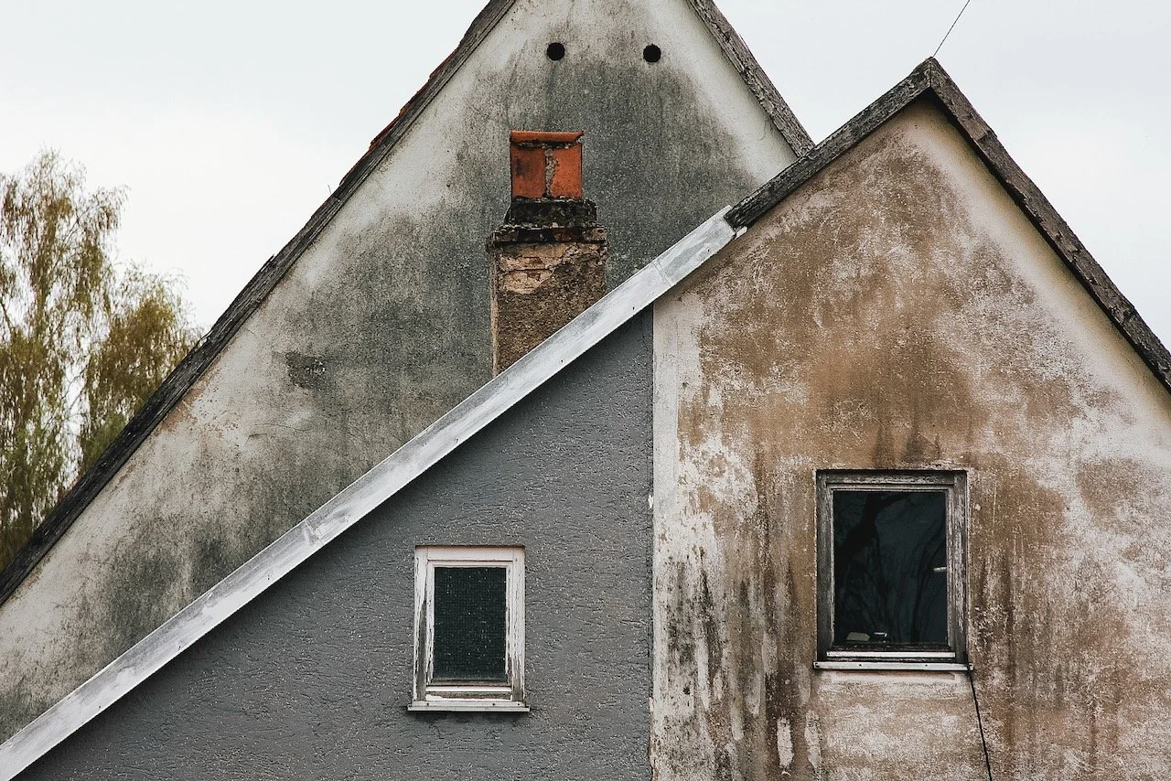 Teil eines alten, zweistöckigen Hauses mit einem schrägen Dach, einer verfallenen Fassade und zwei Fenstern, eines auf jeder Etage.
