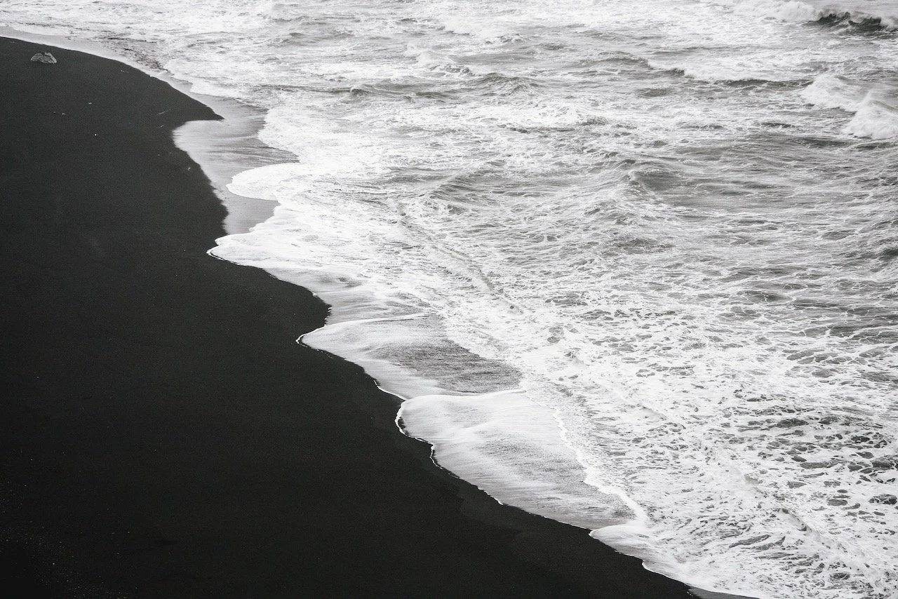 Strand mit schwarzen Sand und wehende Wellen im Meer