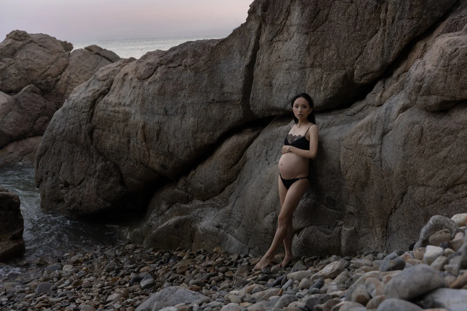 Editorial maternity portrait photographed outdoors by Kay Lai Studio in Hong Kong. The mother-to-be poses by the water in a scenic outdoor location, capturing an elegant and timeless editorial moment.