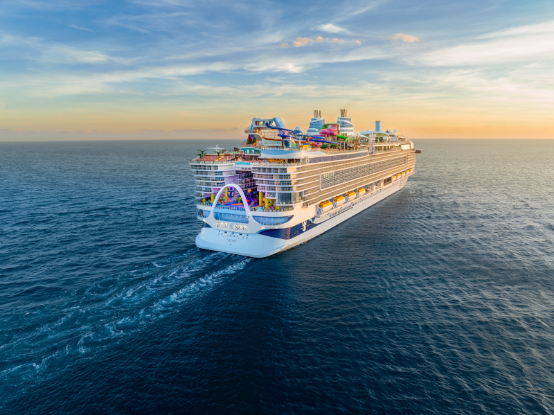 A large cruise ship sailing on the ocean during sunset, with colorful water slides and recreational areas on the top deck.