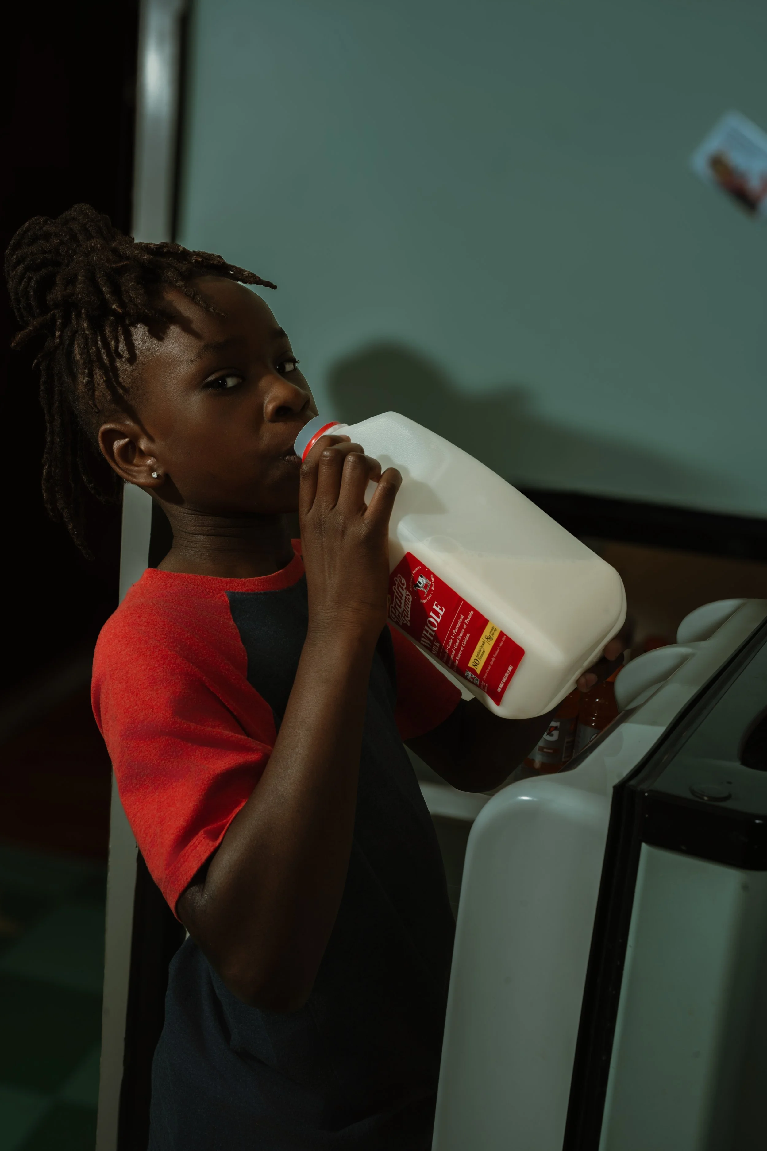 A young girl with braided hair drinking milk from a jug at a vending machine.