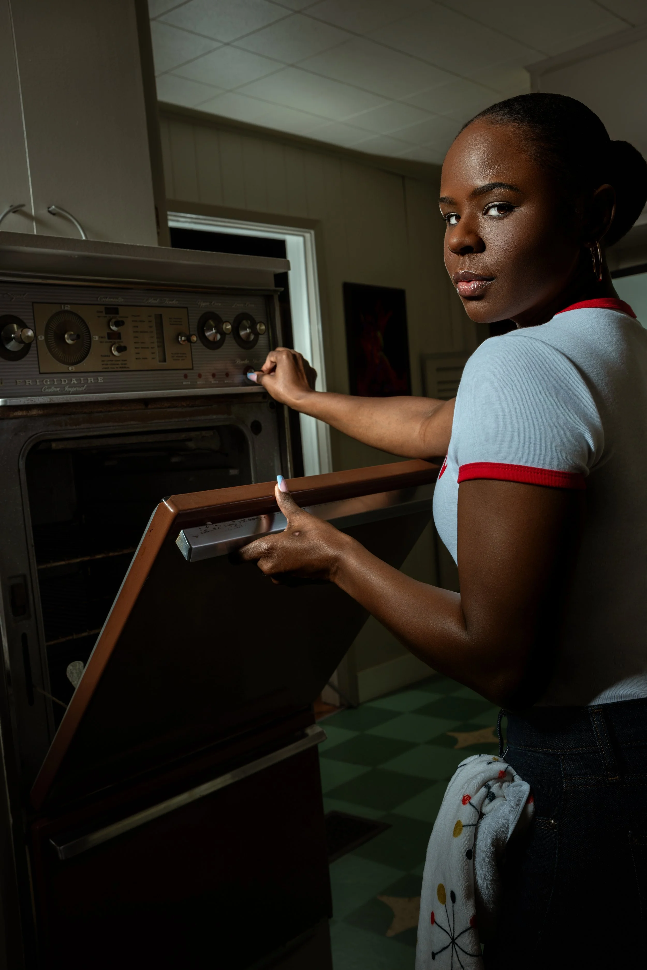 A woman adjusting a vintage oven in a kitchen with a towel hanging from her pocket.