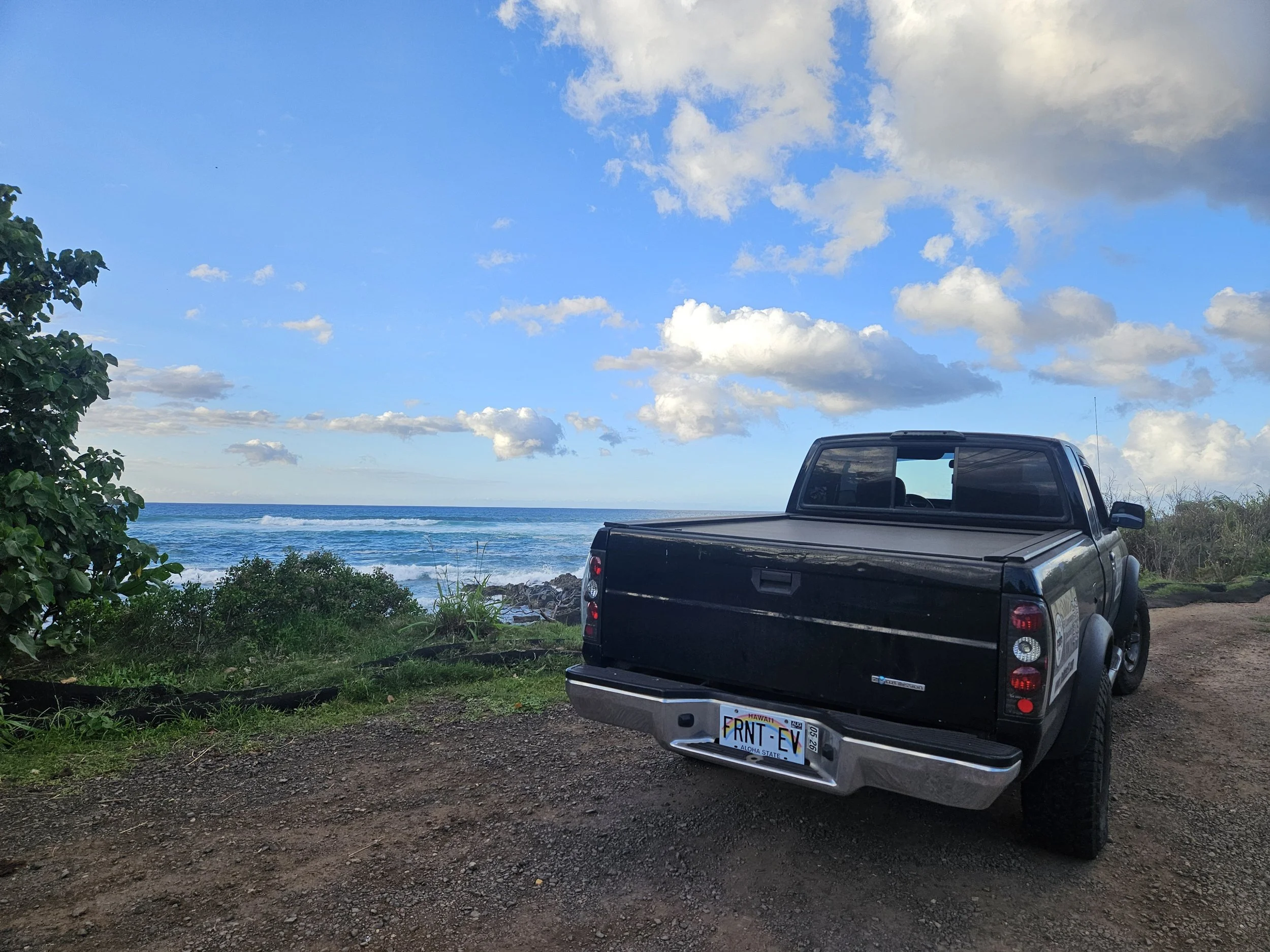 Black pickup on dirt parking by rocky shoreline