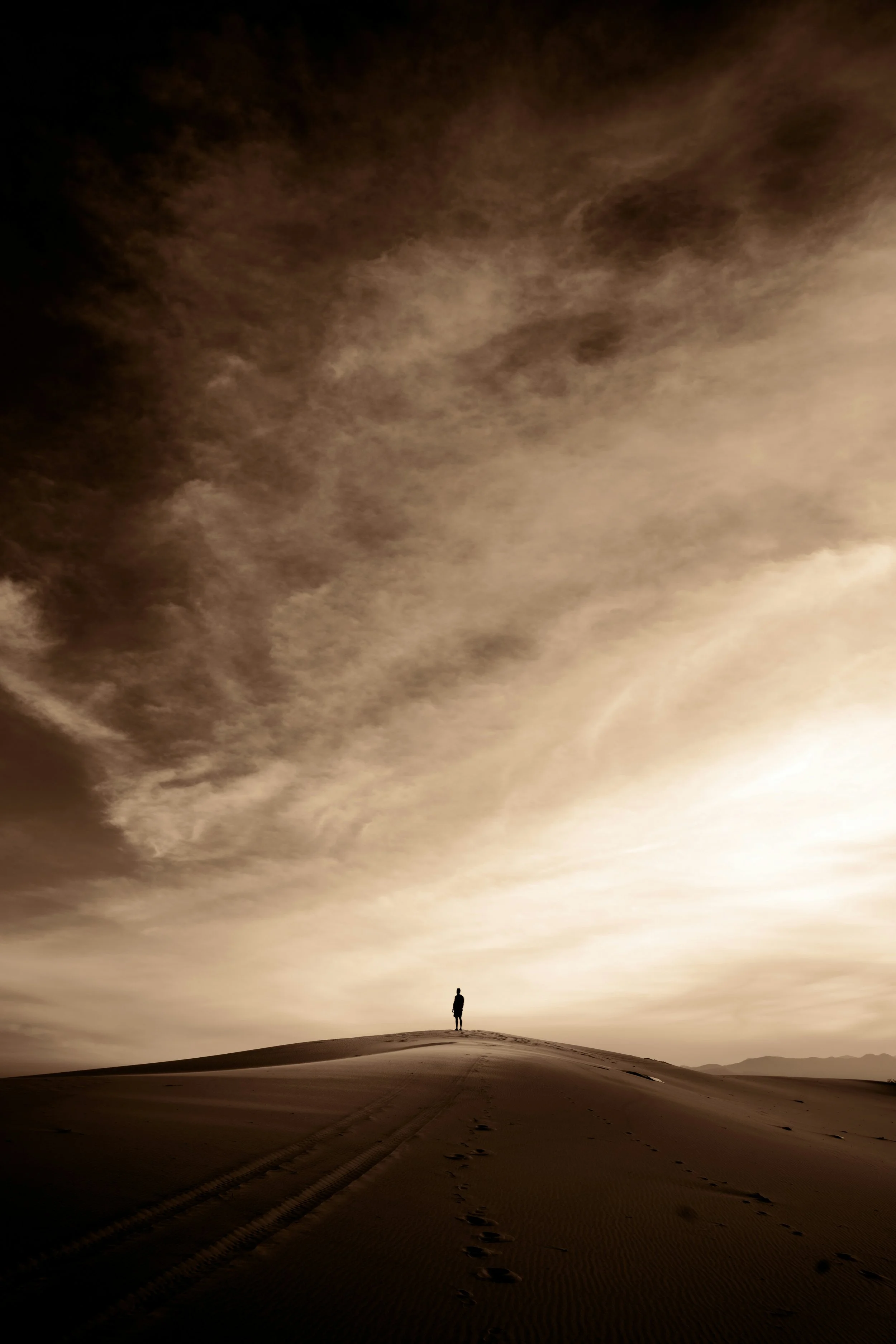 Silhouette of a person standing alone on a sand dune under dramatic skies, symbolizing solitude and spiritual awakening.