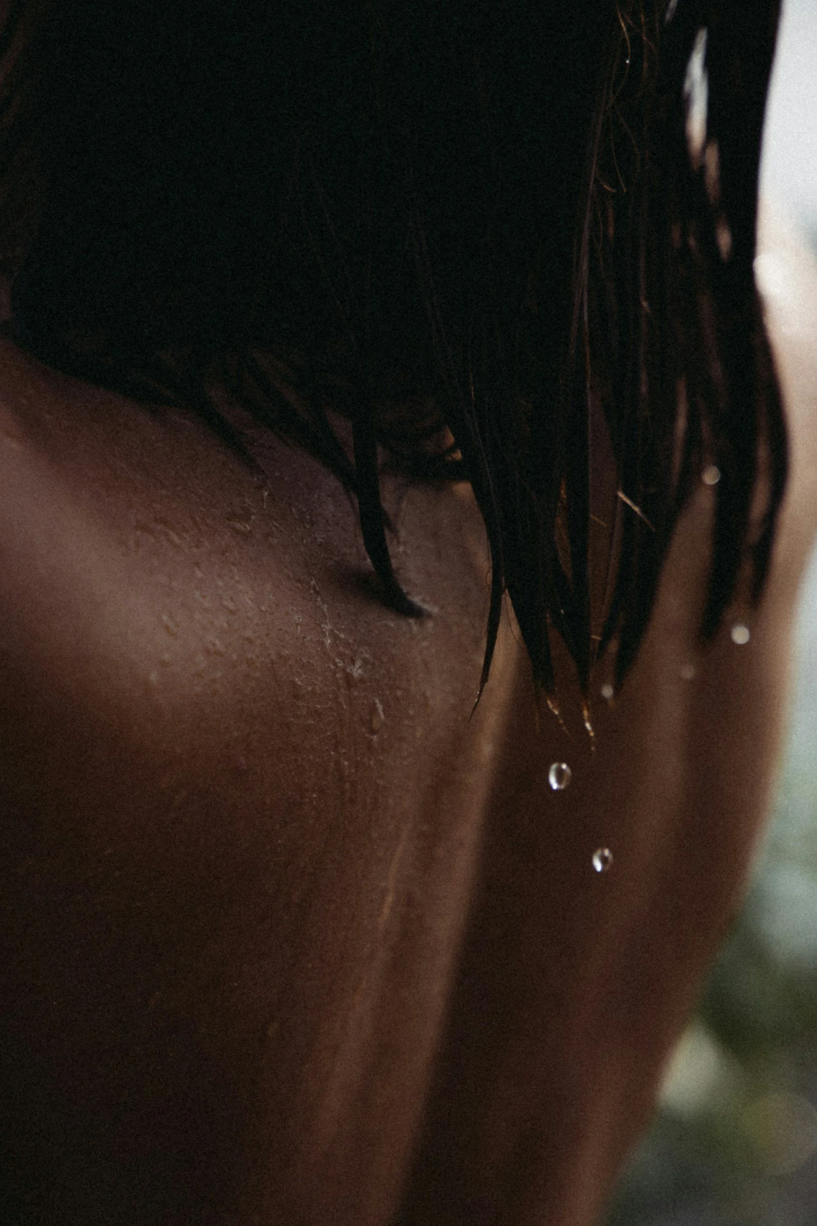 Close-up of a person with wet skin, dark hair, and water droplets on their shoulder.