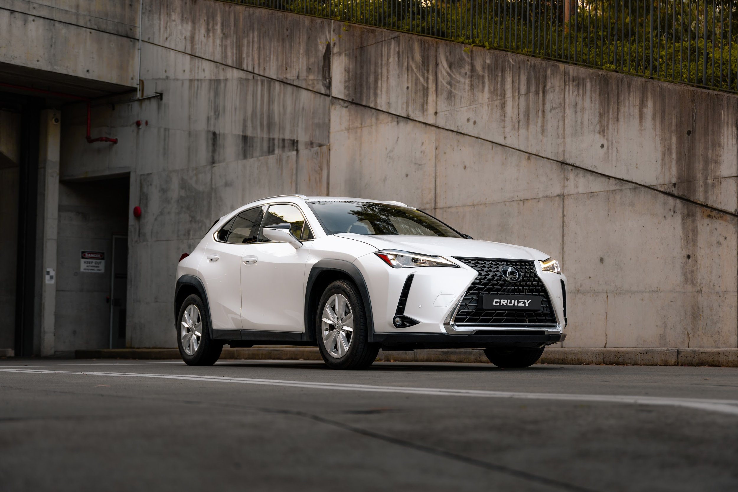 White Lexus SUV parked in front of a concrete wall with a metal railing above.