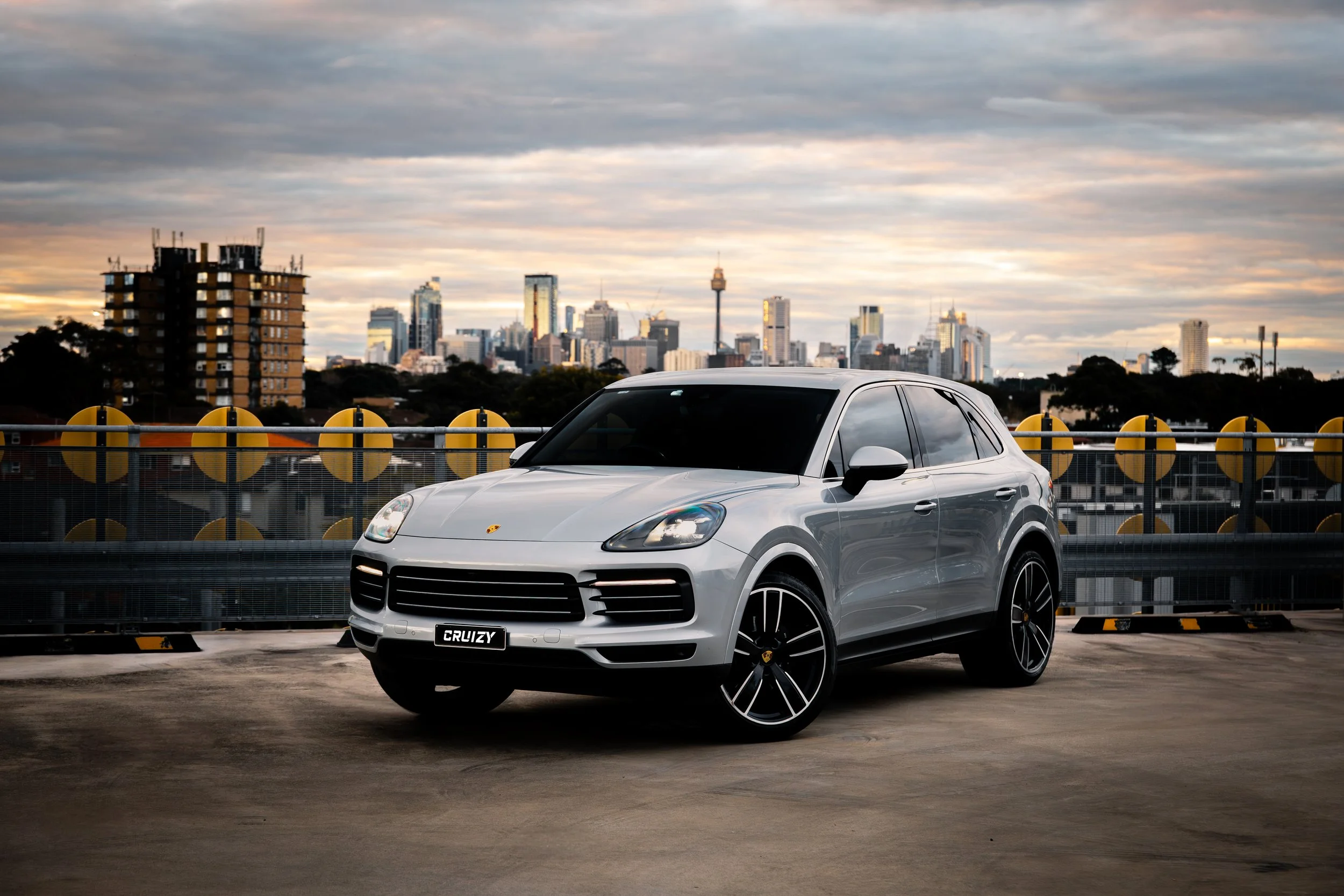 A white luxury SUV parked on a rooftop parking lot with a city skyline in the background during sunset.