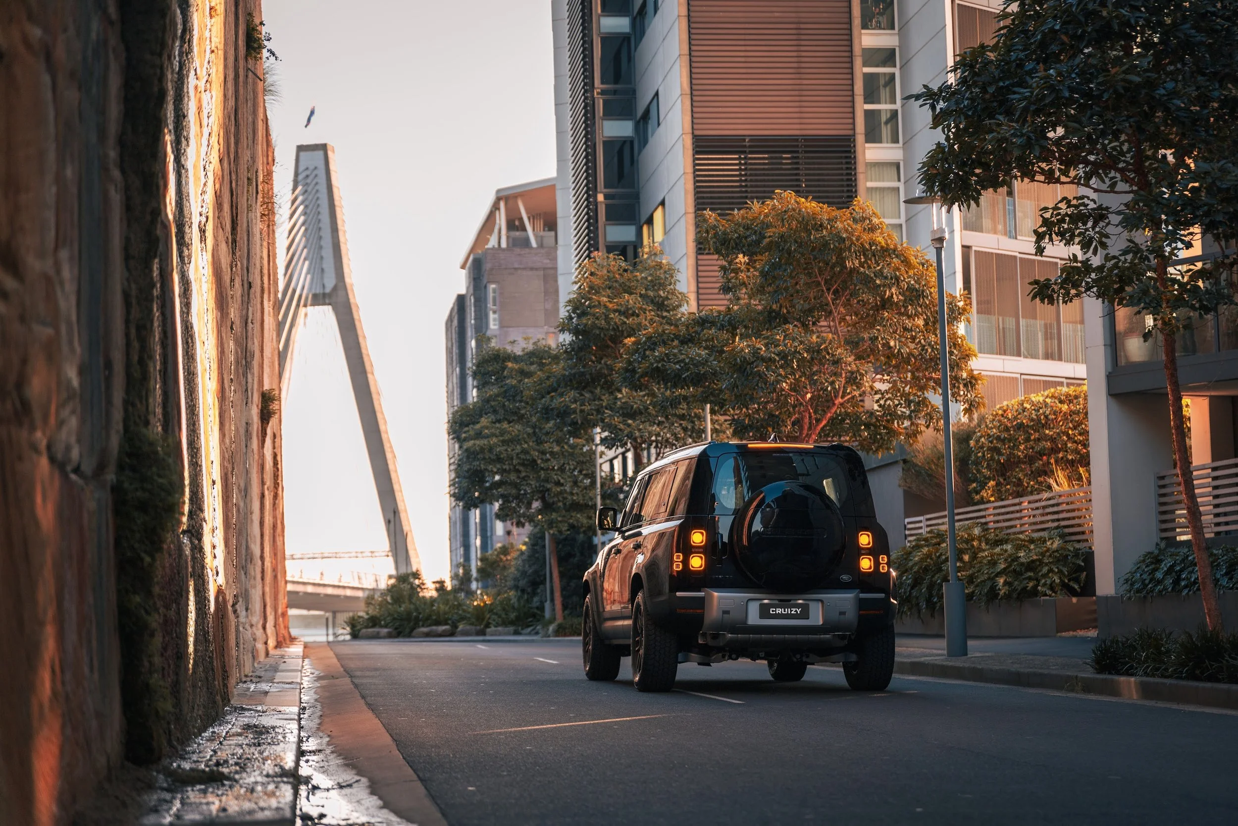 Black SUV parked on a city street during sunset with modern high-rise buildings and trees around.