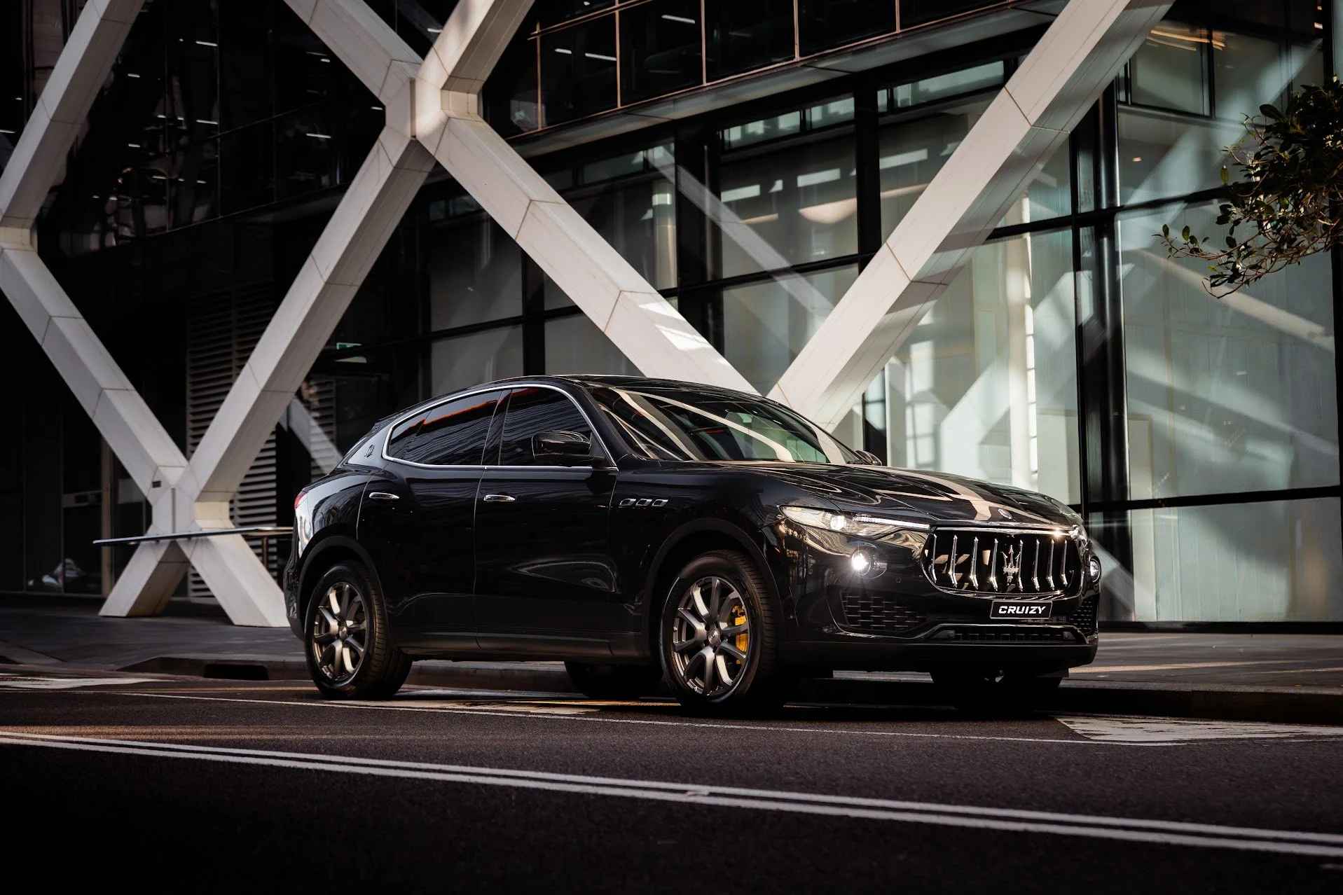 A black Maserati SUV parked on a city street at night in front of a modern building with large glass windows and white architectural beams.