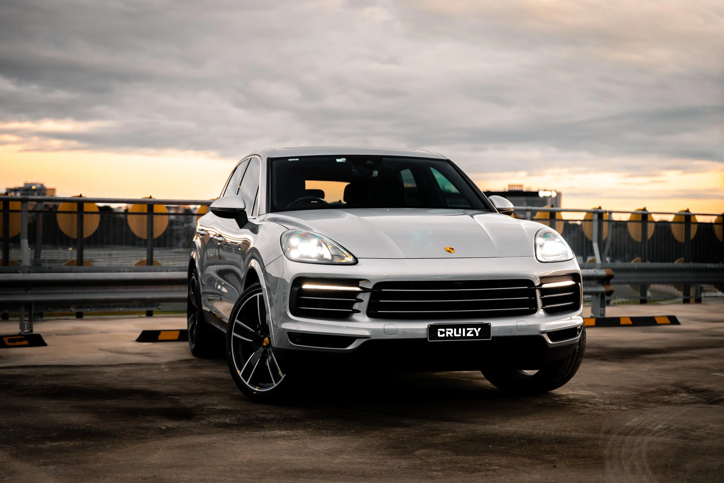 A white luxury SUV parked on an upper level parking garage at sunset with a city skyline in the background.