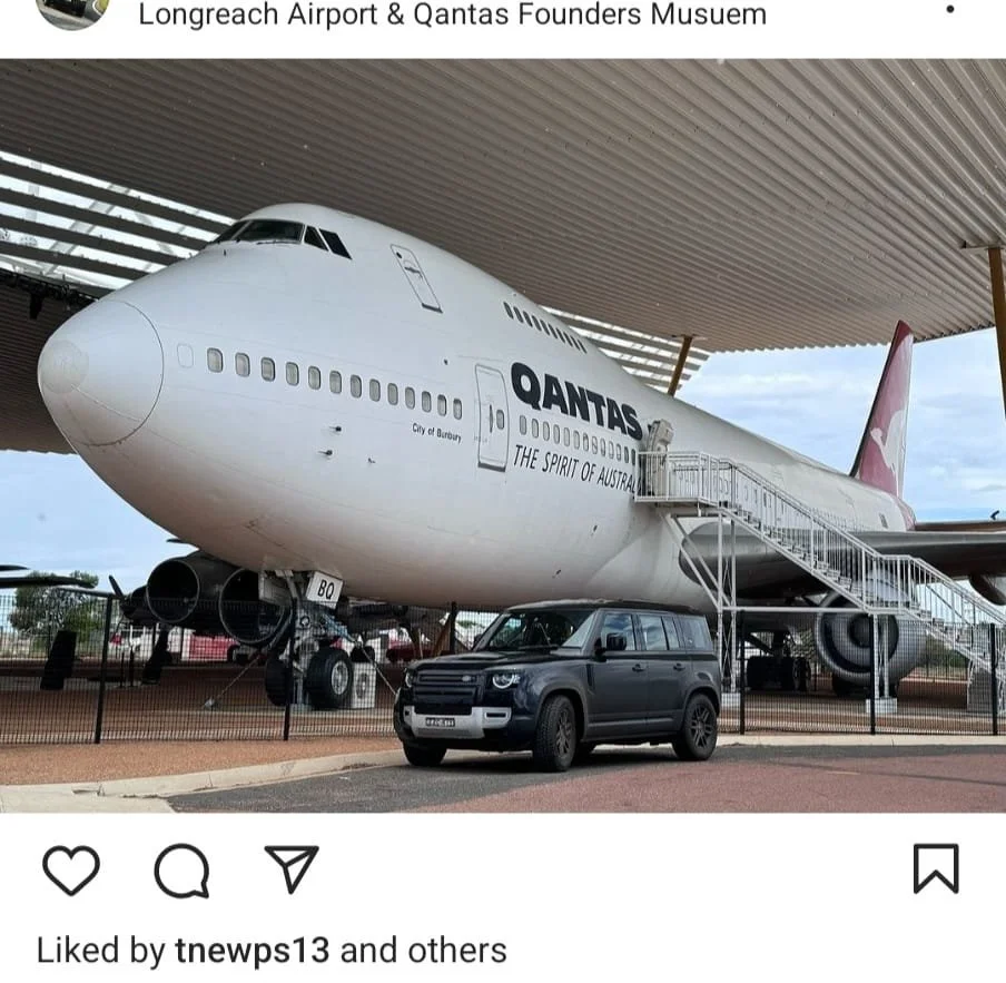 A large airplane with Qantas branding on display at a museum, with a staircase leading up to the entrance and a black vehicle parked underneath.