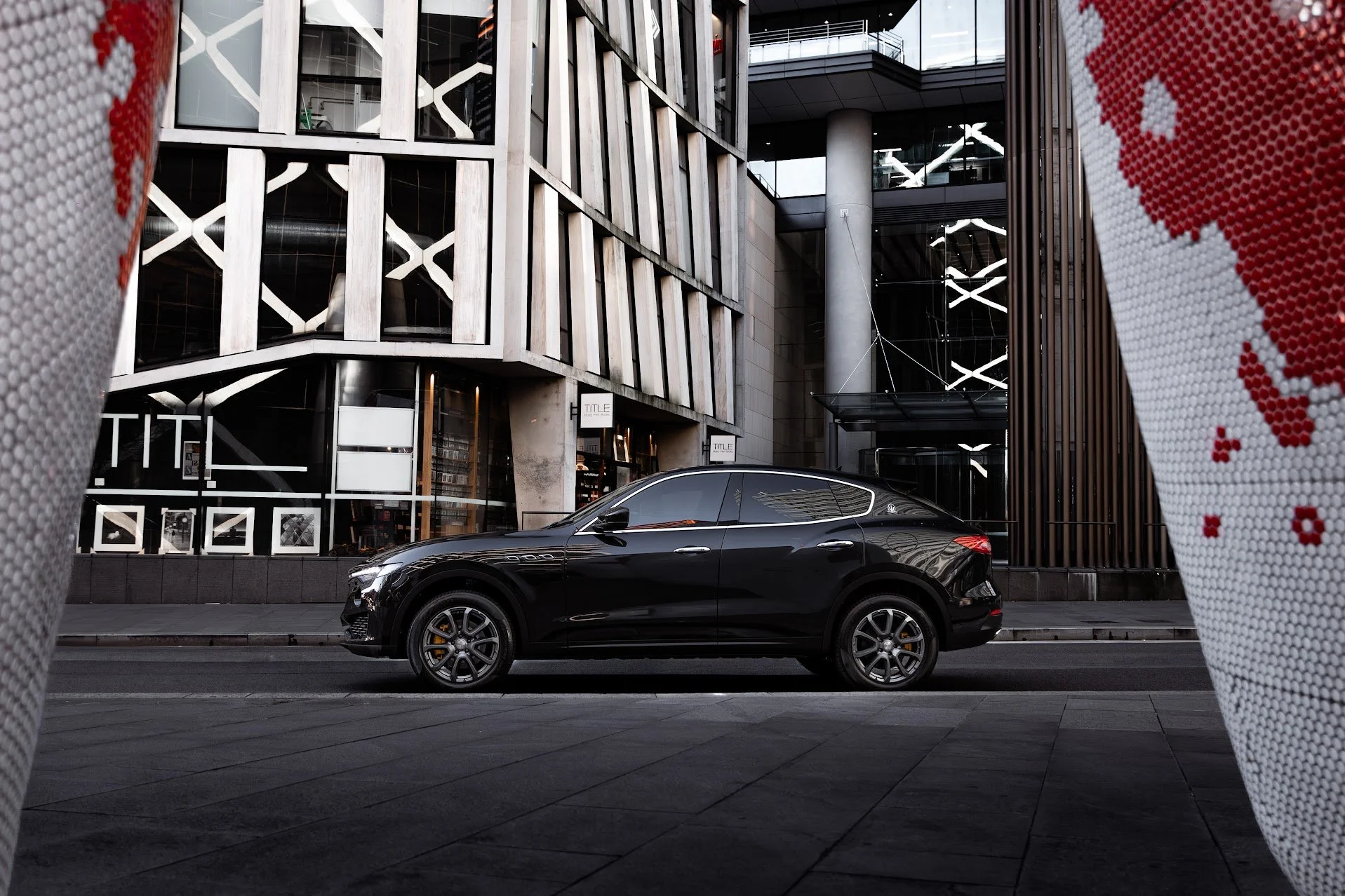A black luxury sedan car parked on an urban street with modern buildings in the background.