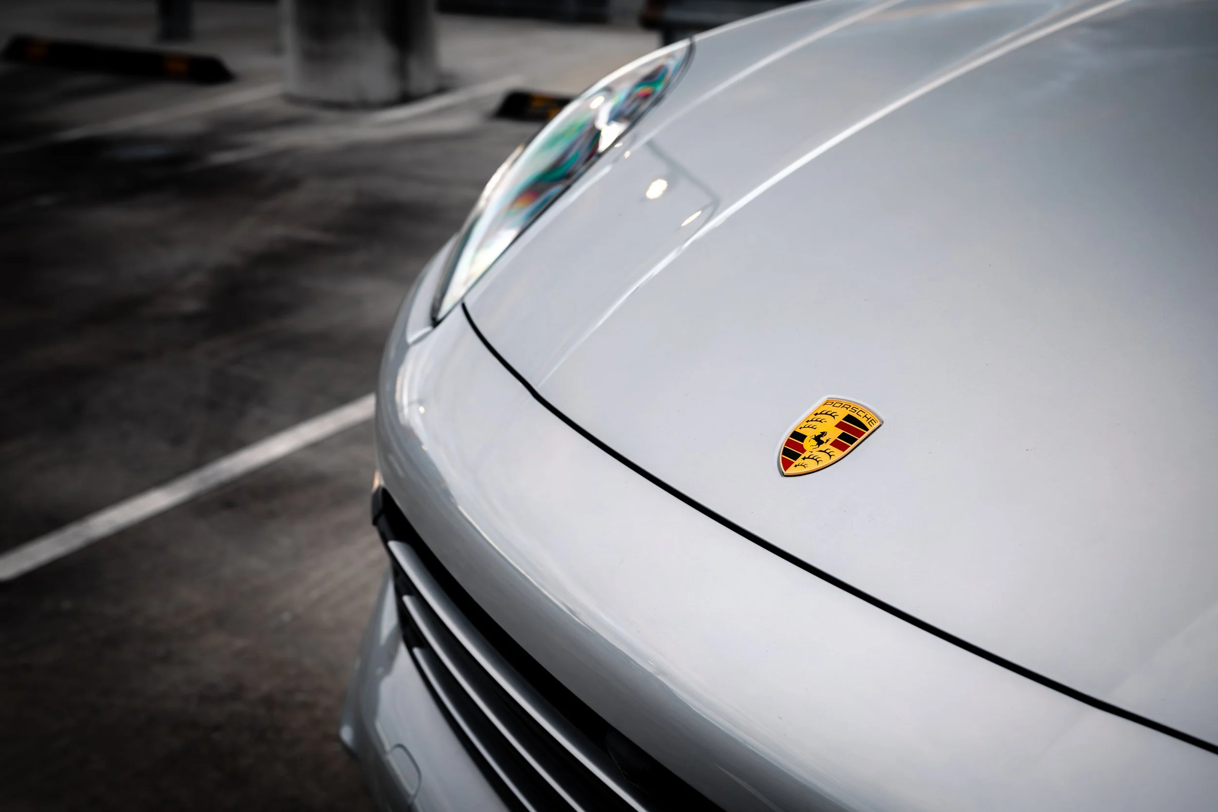 Close-up of a white Porsche car with the Porsche emblem on the hood, parked in a parking lot.