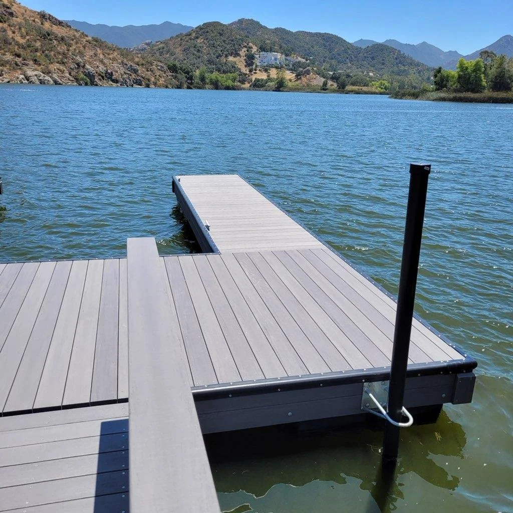 A wooden dock extends out into a lake surrounded by mountains and trees.