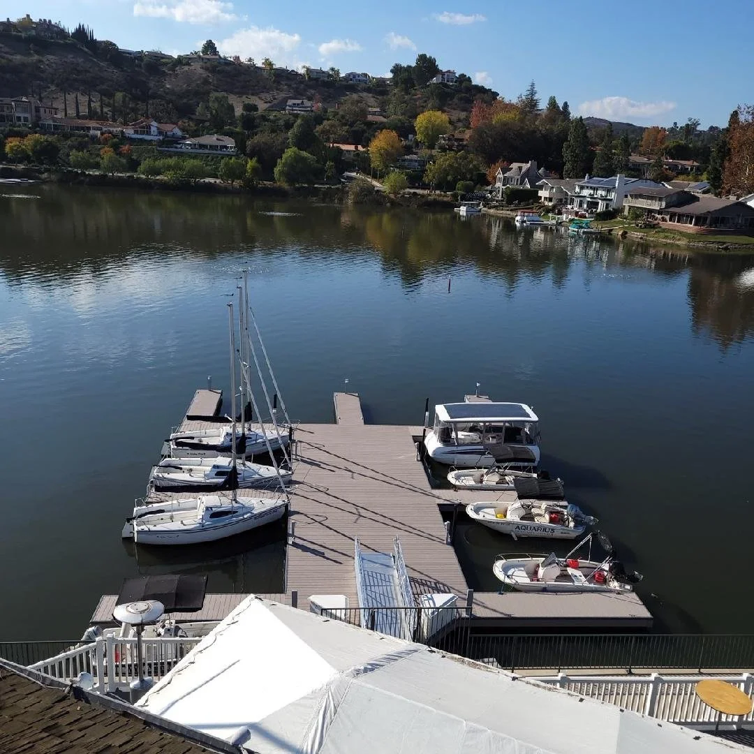 A dock with several boats moored on calm water, overlooking colorful trees and houses on a hillside.
