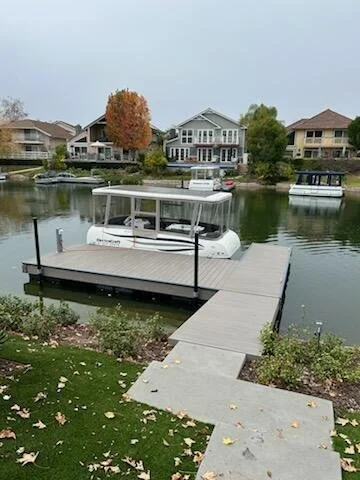 Dock with a boat moored on a canal, with houses and trees in the background.