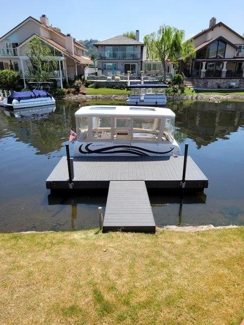 A white boat docked at a floating pier on a calm waterway with houses and palm trees in the background.
