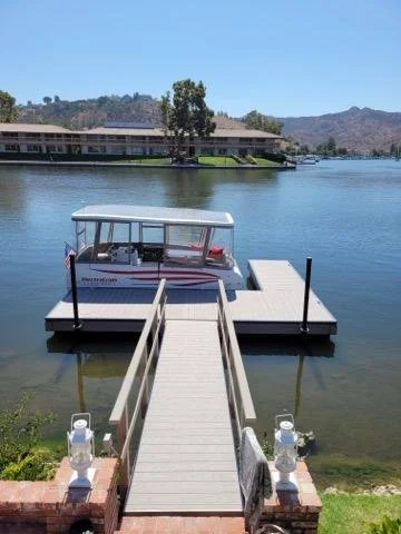 Dock extending into a lake with a boat tied at the end, houses and hills in the background.