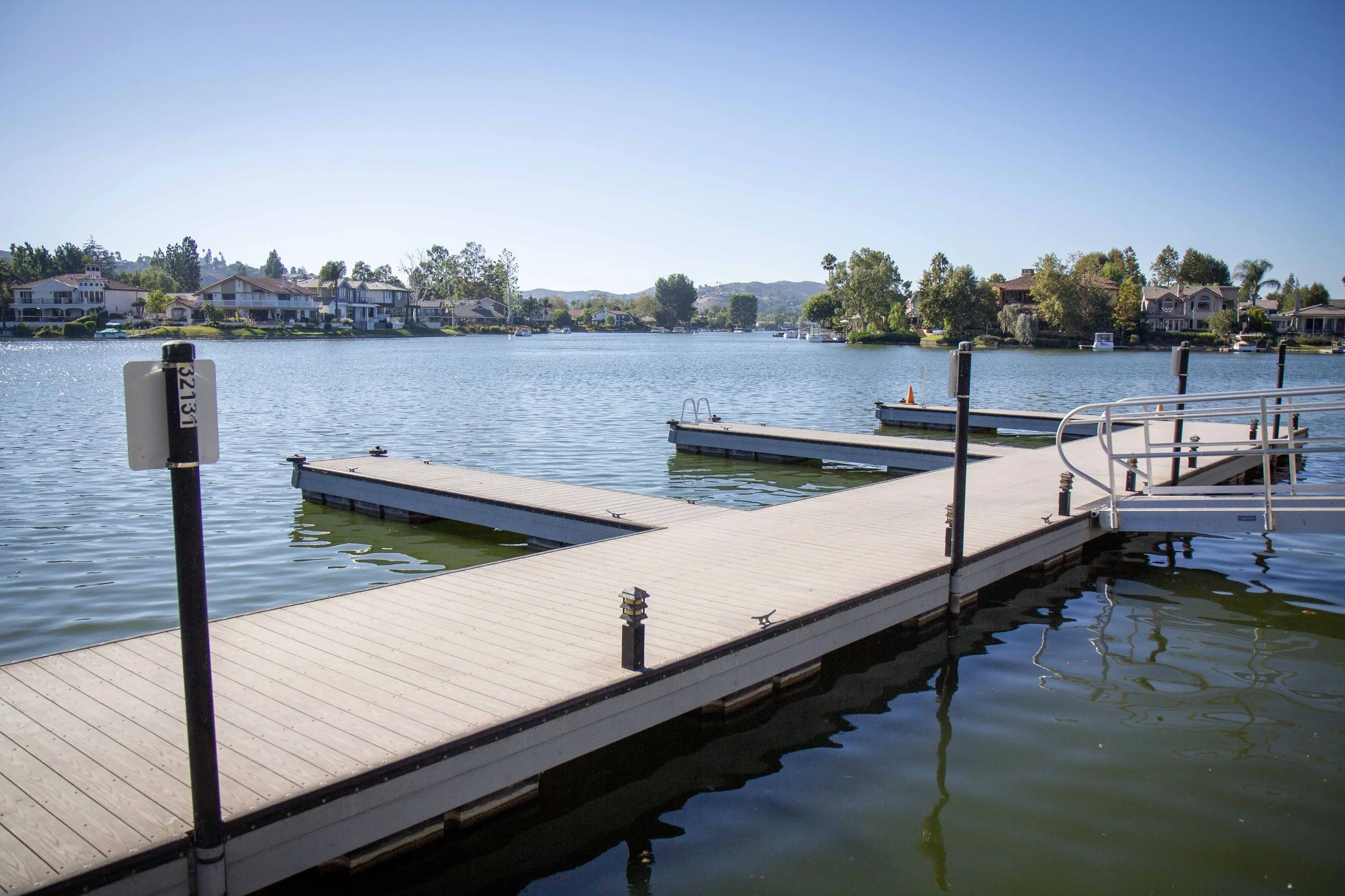 Dock extending into calm lake with houses and trees in the background under clear blue sky.