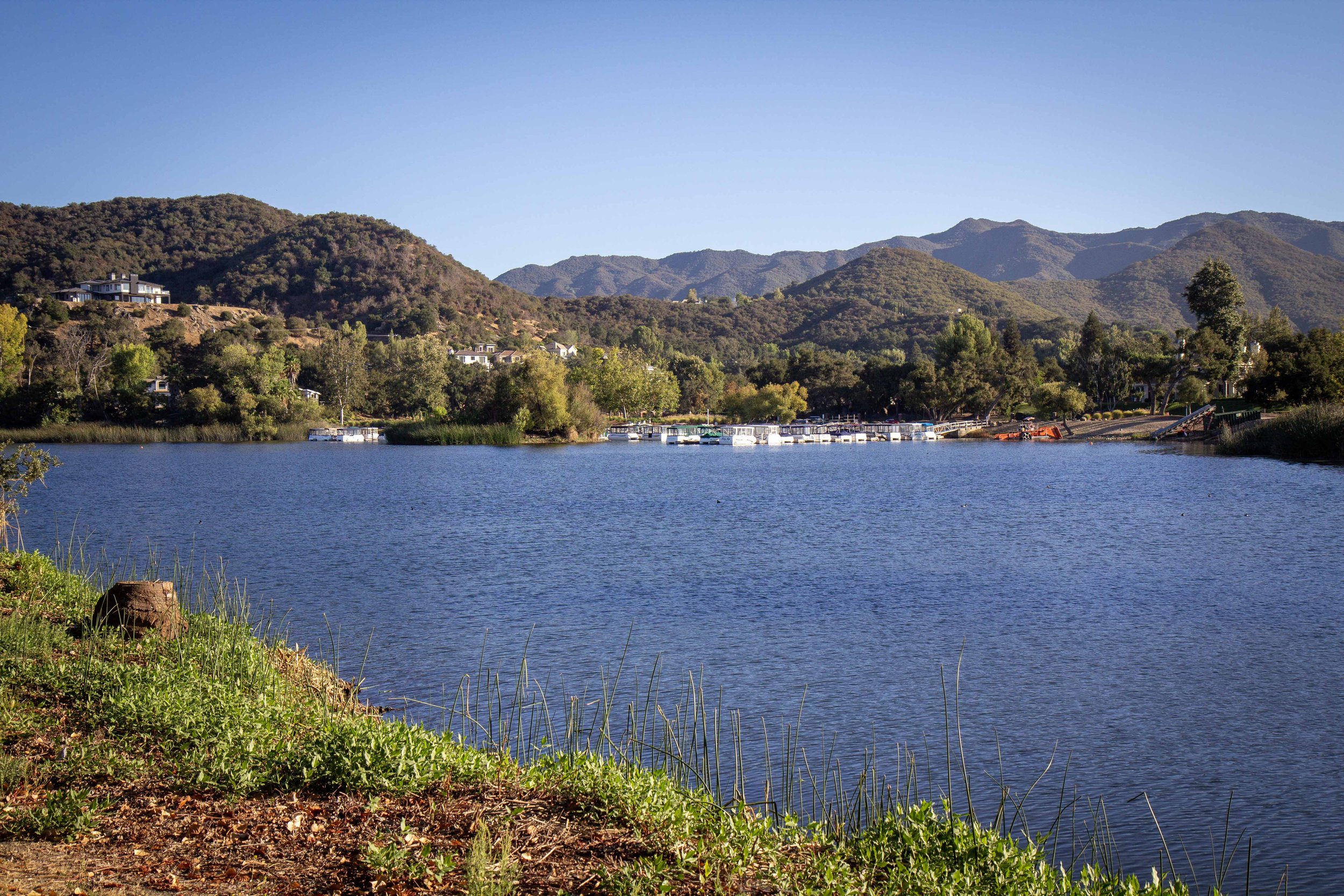 A peaceful lake surrounded by green trees and hills under a clear blue sky.