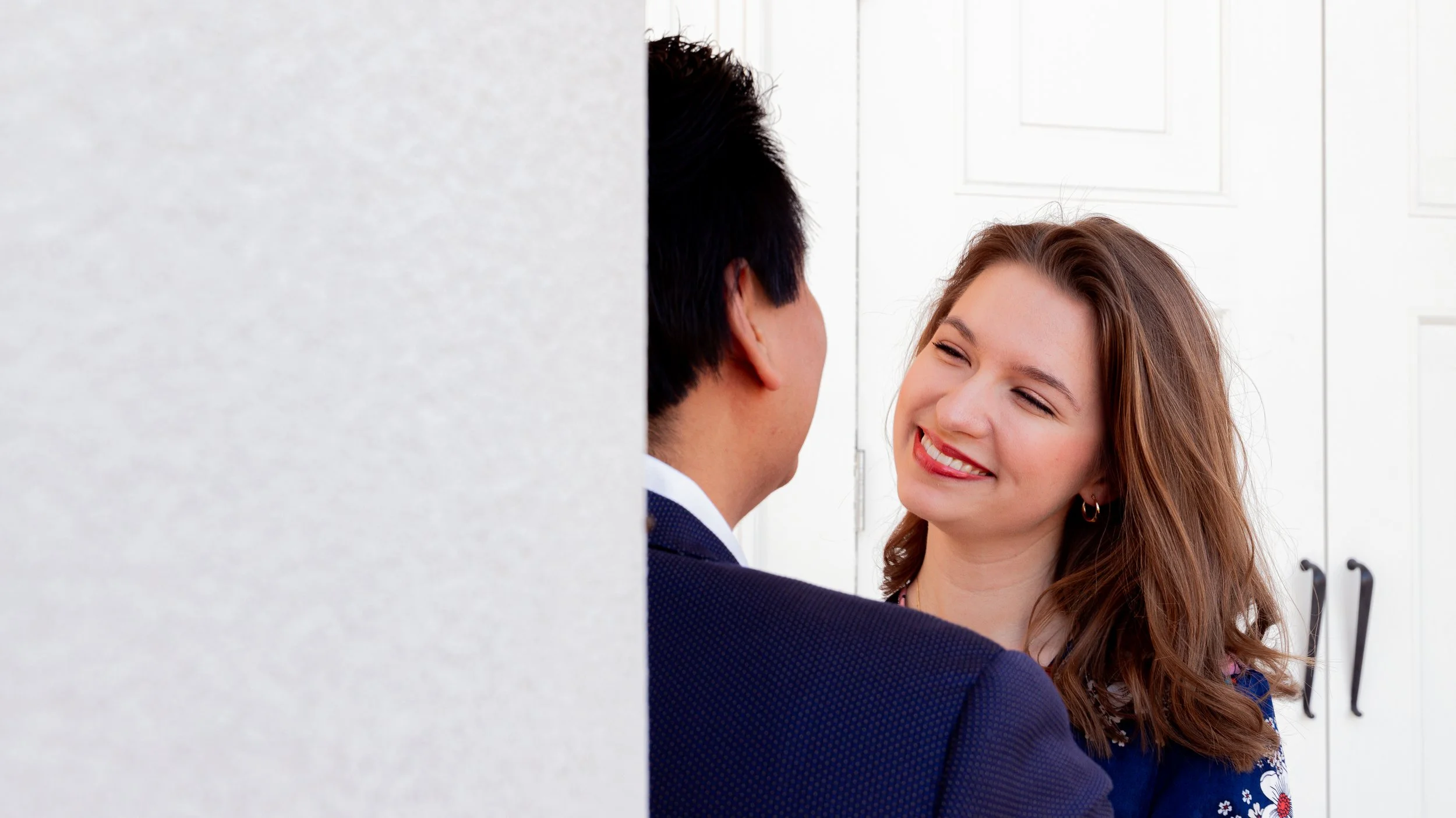 A woman with red hair smiling at a man, partly visible, in front of white cabinets.