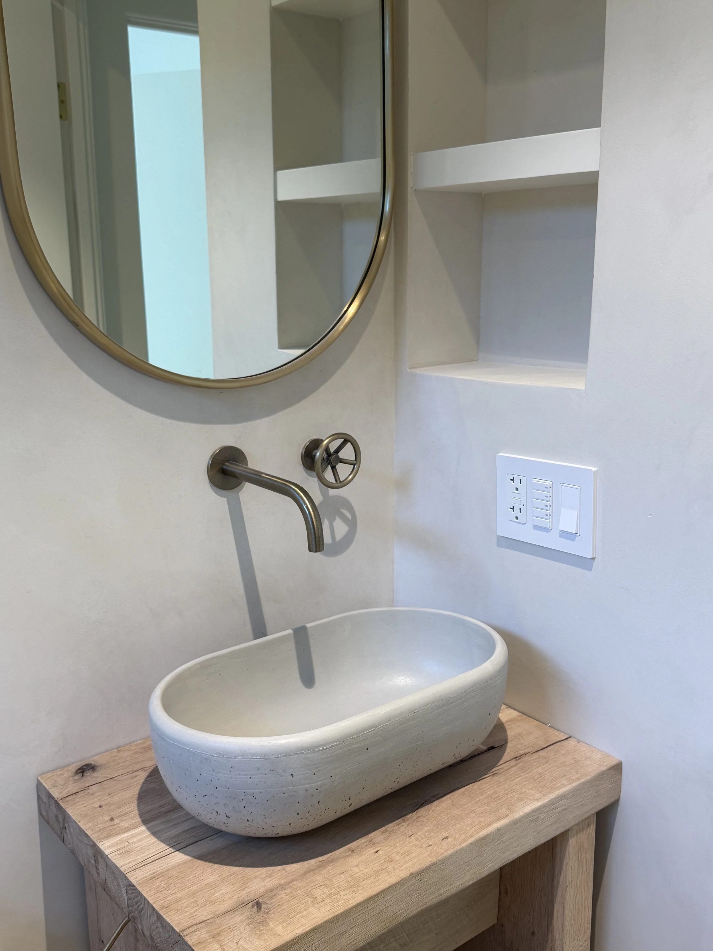 Tadelakt plaster Bathroom walls, sink with a large round mirror, open shelves, a wall-mounted faucet, and a wooden countertop.