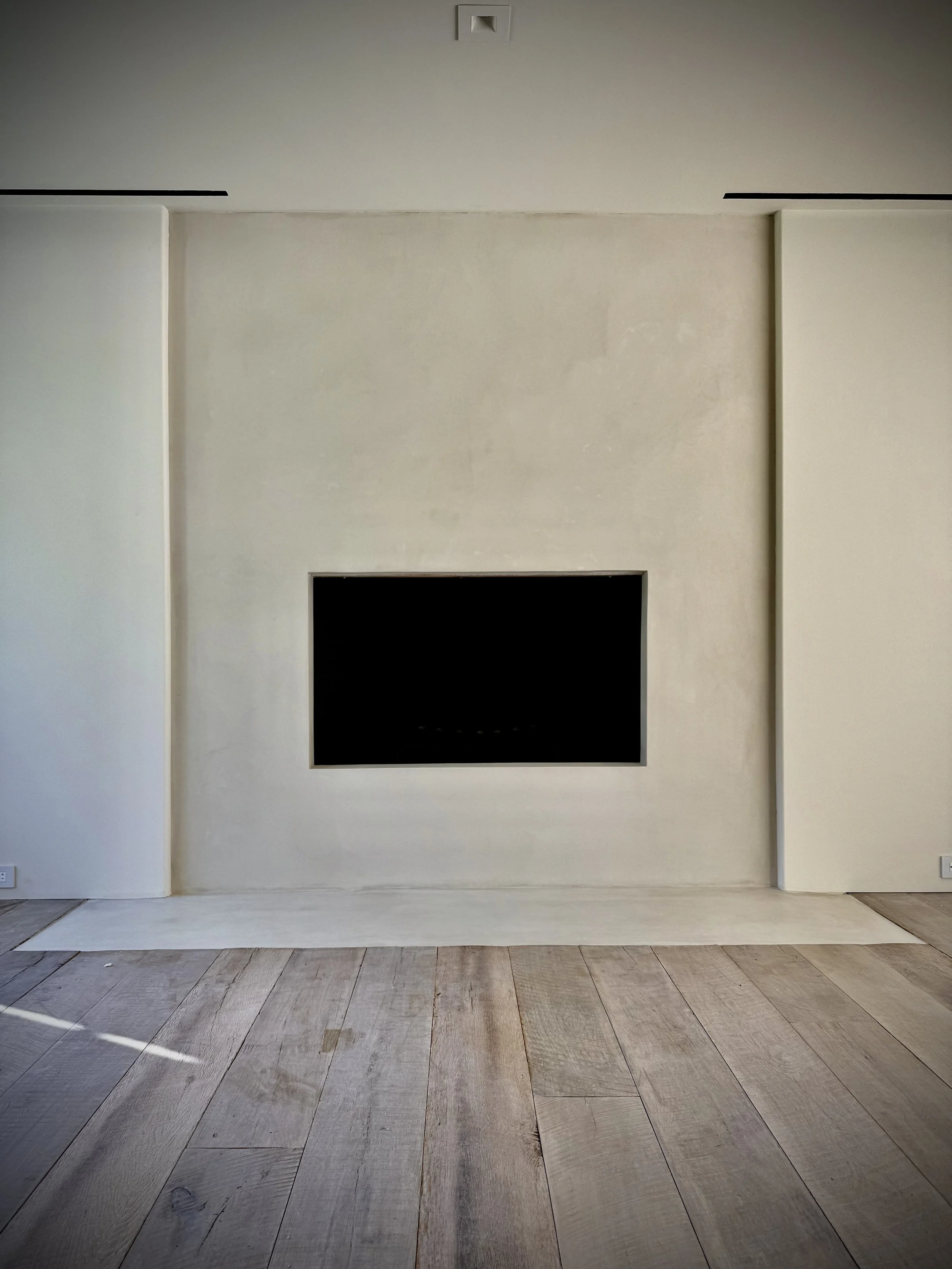 Tadelakt plaster fireplace, neutral-colored walls, wood flooring, and a recessed area in the ceiling.