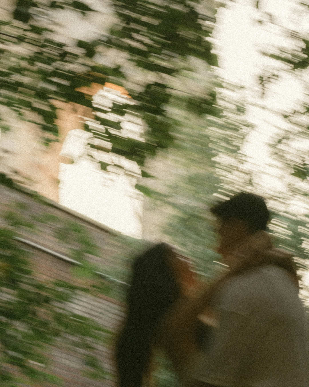 A blurry photo of a couple kissing outdoors, with trees and a building in the background.