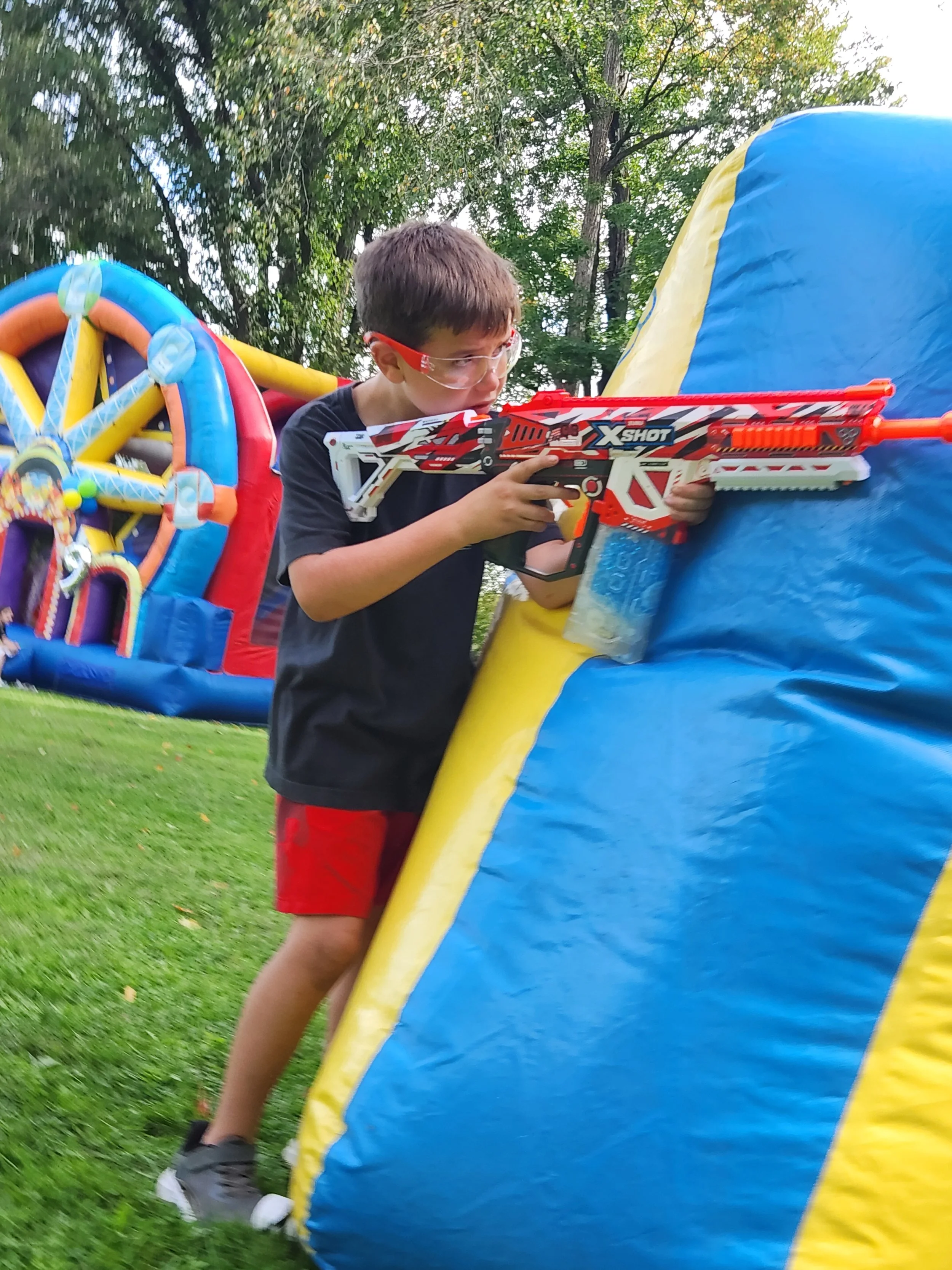 A young boy firing a toy dart gun at an inflatable target outdoors.
