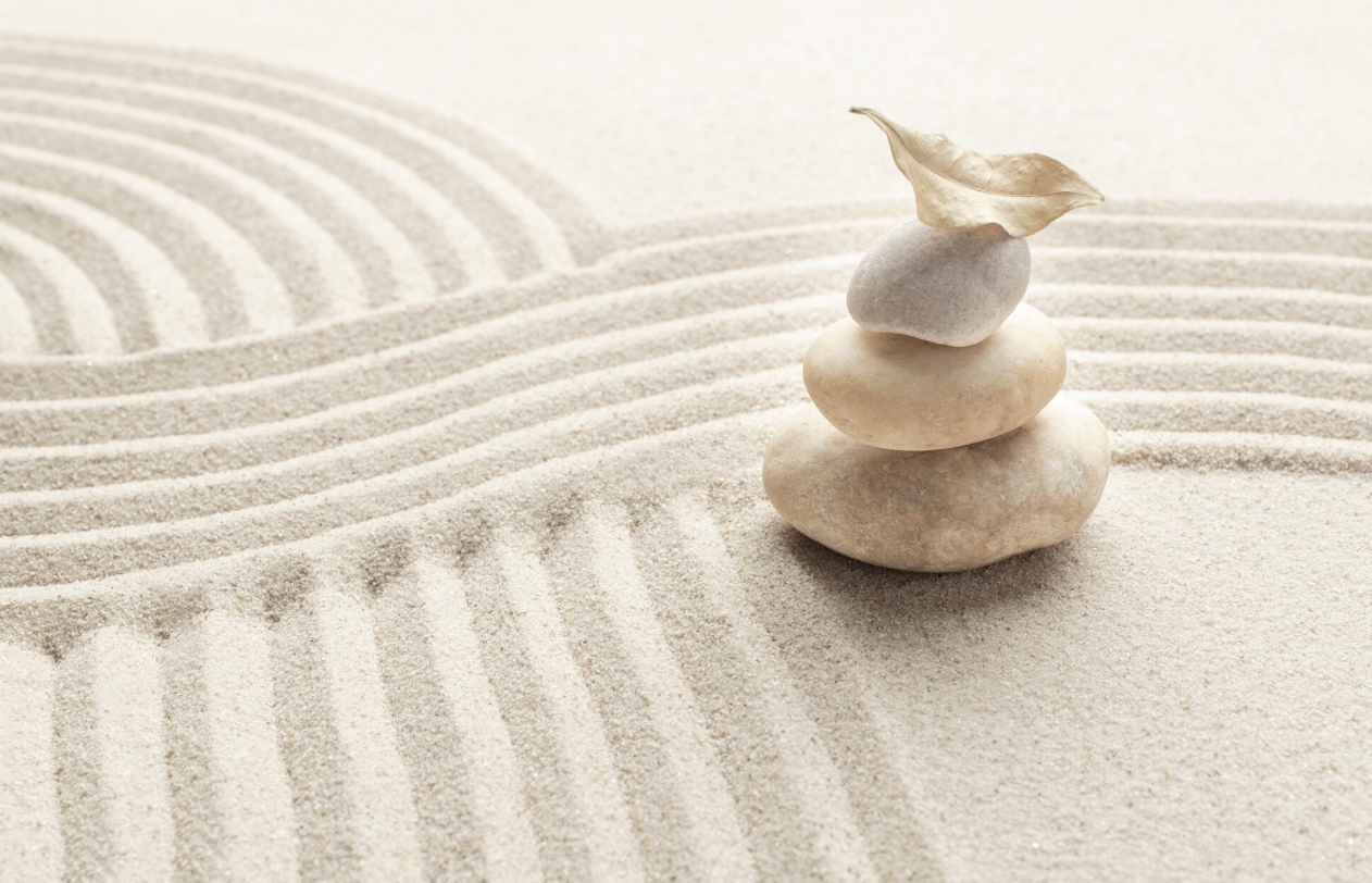 Sand arranged in a zen garden with three stacked stones and a leaf on top