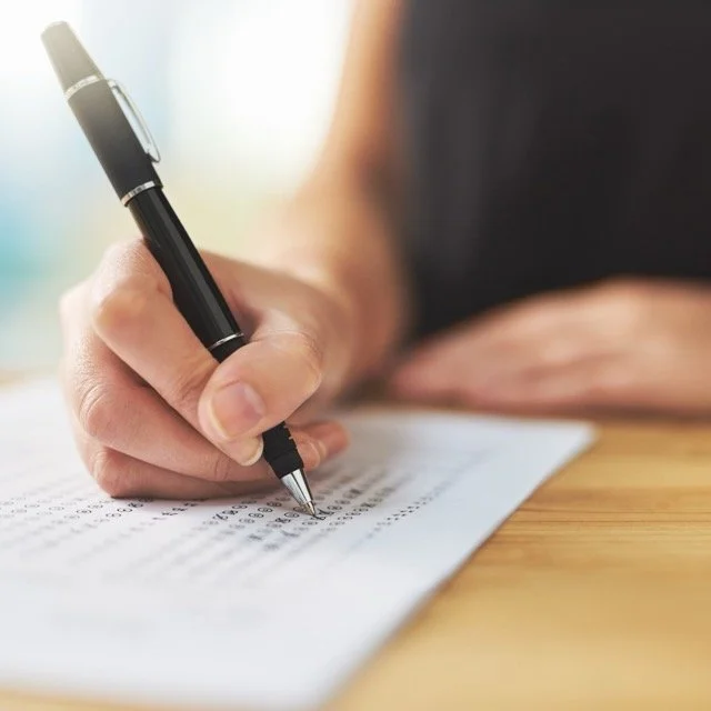 A person filling out a multiple-choice answer sheet with a black pen.