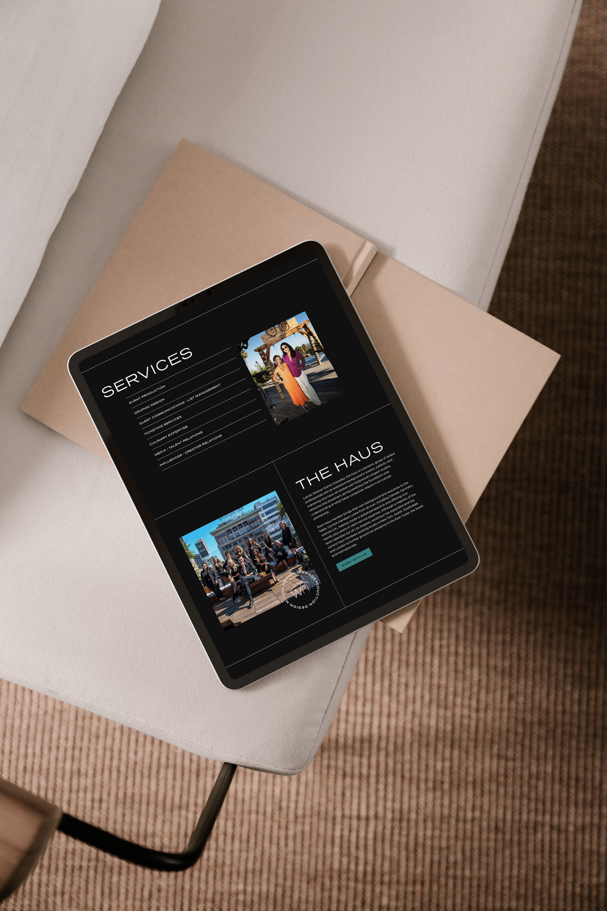 Digital tablet displaying a website with services and a group photo on a light-colored cushioned surface, with a beige closed laptop underneath.