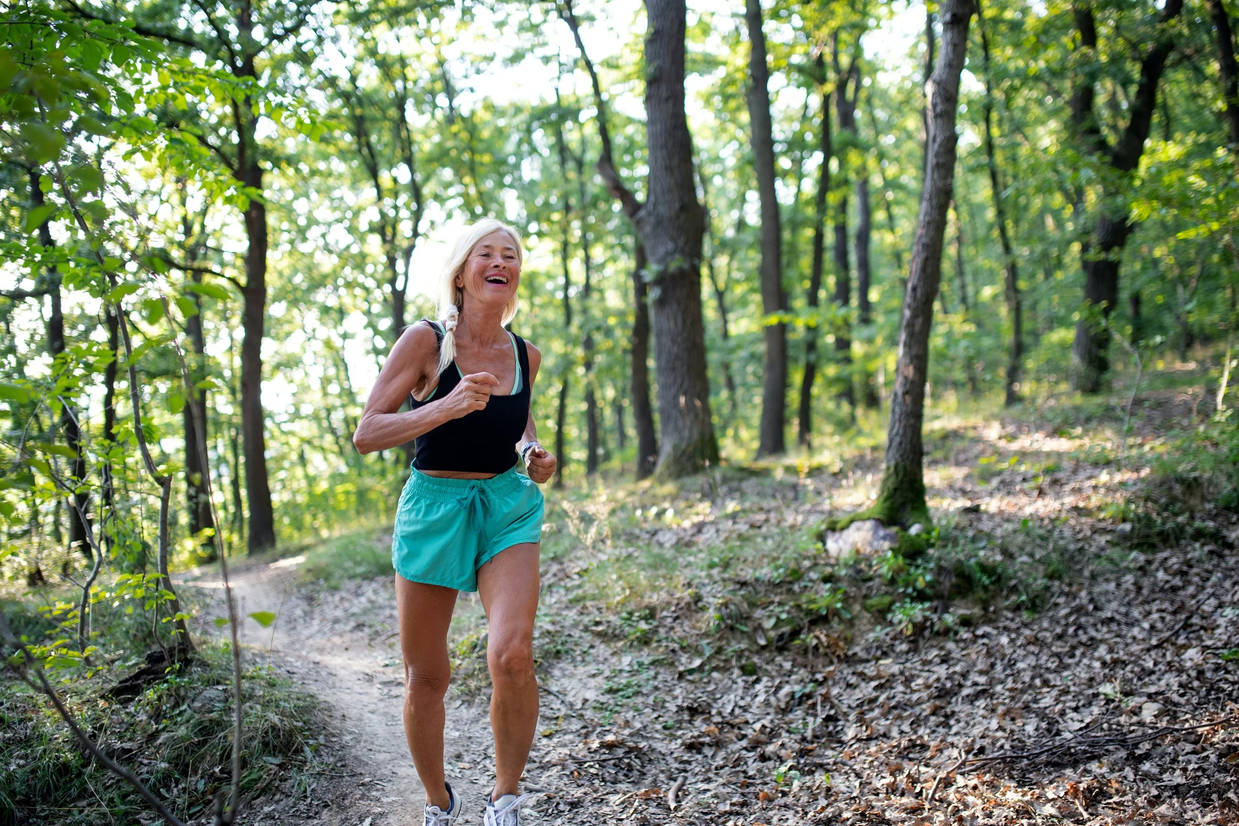 Smiling woman running on a wooded trail, staying active after PulseWave acoustic wave therapy at Hiller Wellness in Southern Pines, NC