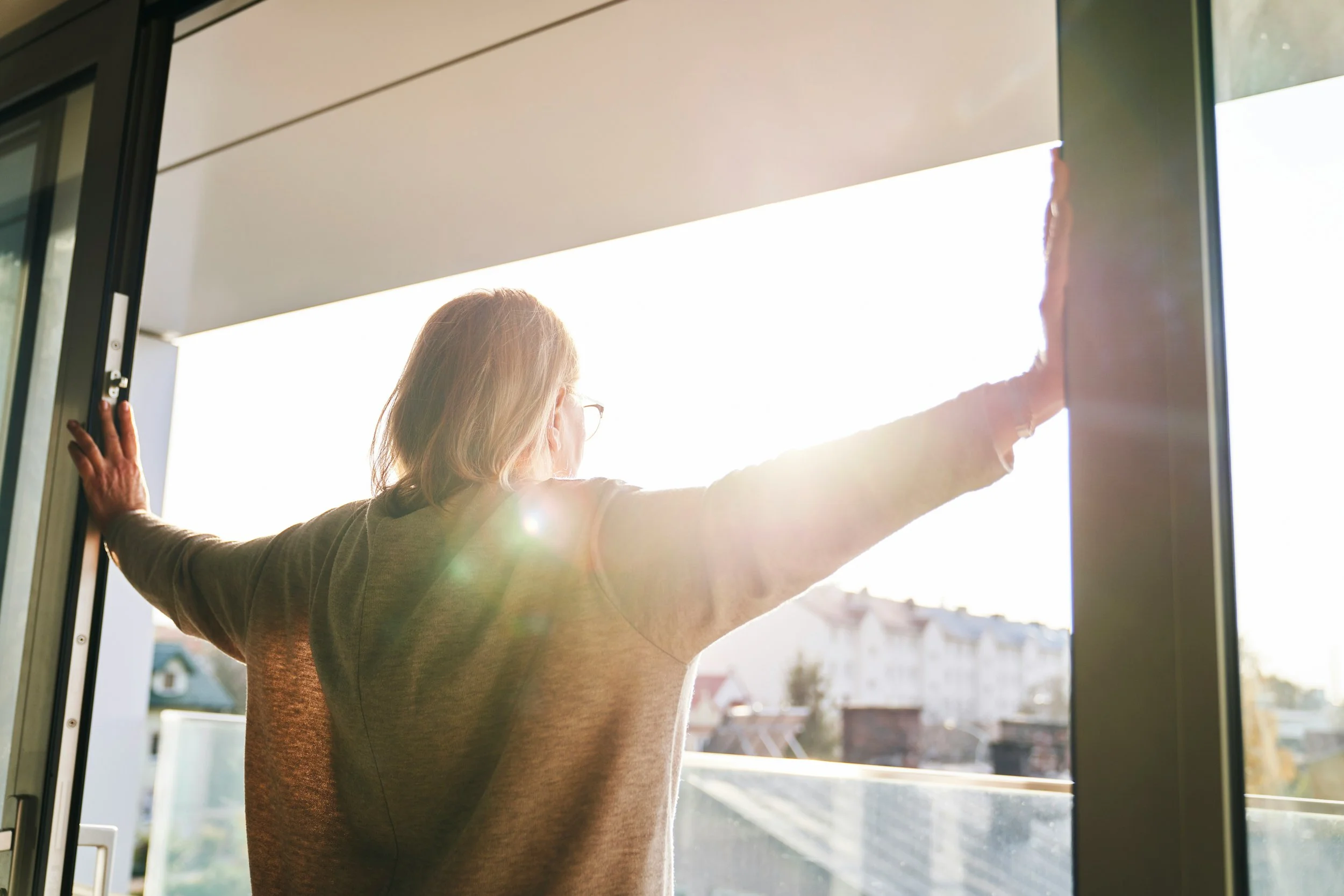 Woman opening a door to bright morning sunlight, feeling refreshed after infrared sauna therapy at Hiller Wellness in Southern Pines, NC
