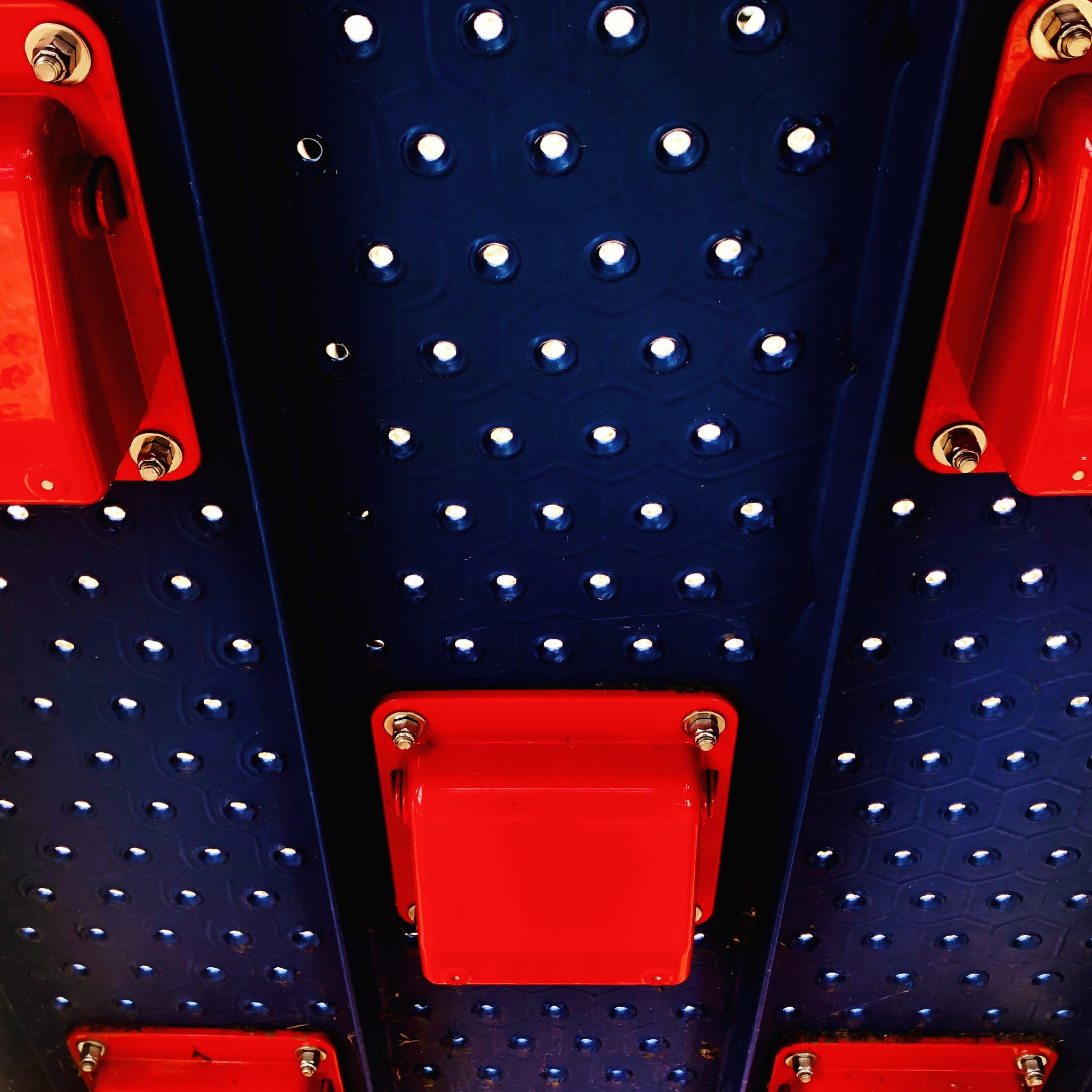 Close-up of a black pegboard with red call boxes and metal bolts.