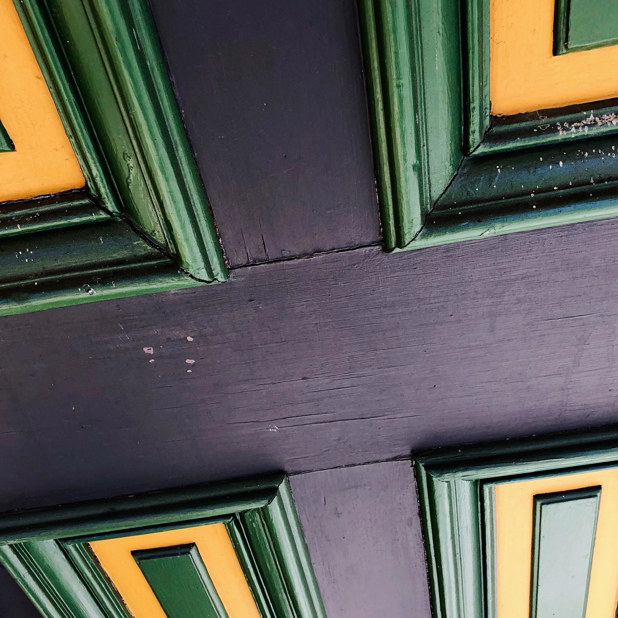 Close-up of a colorful wooden door with green, yellow, and black trim, showing wear and small white paint splatters.
