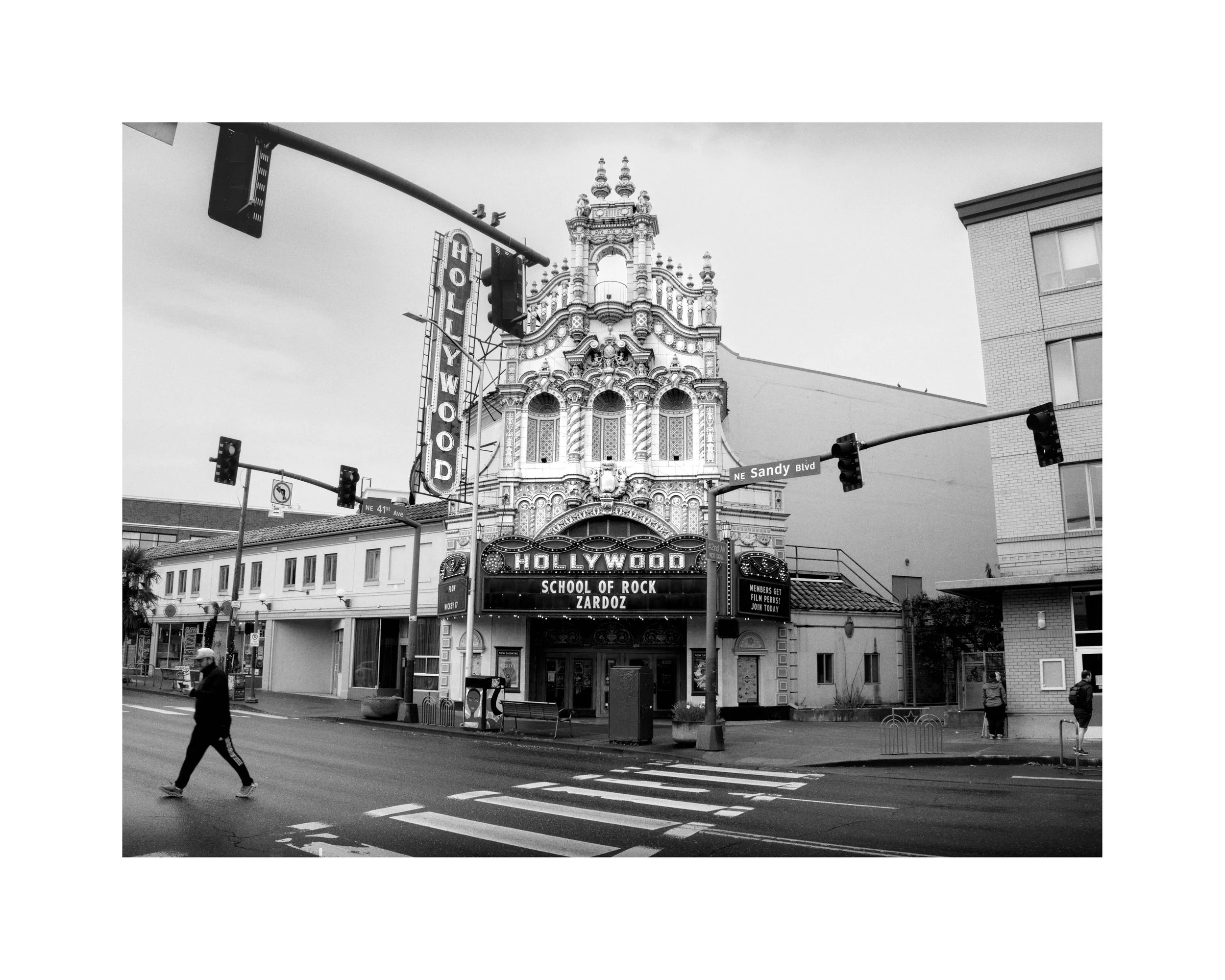 Black and white photo of the Hollywood Theatre in Portland, Oregon, with its ornate facade and neon signage, and a pedestrian crossing the street.