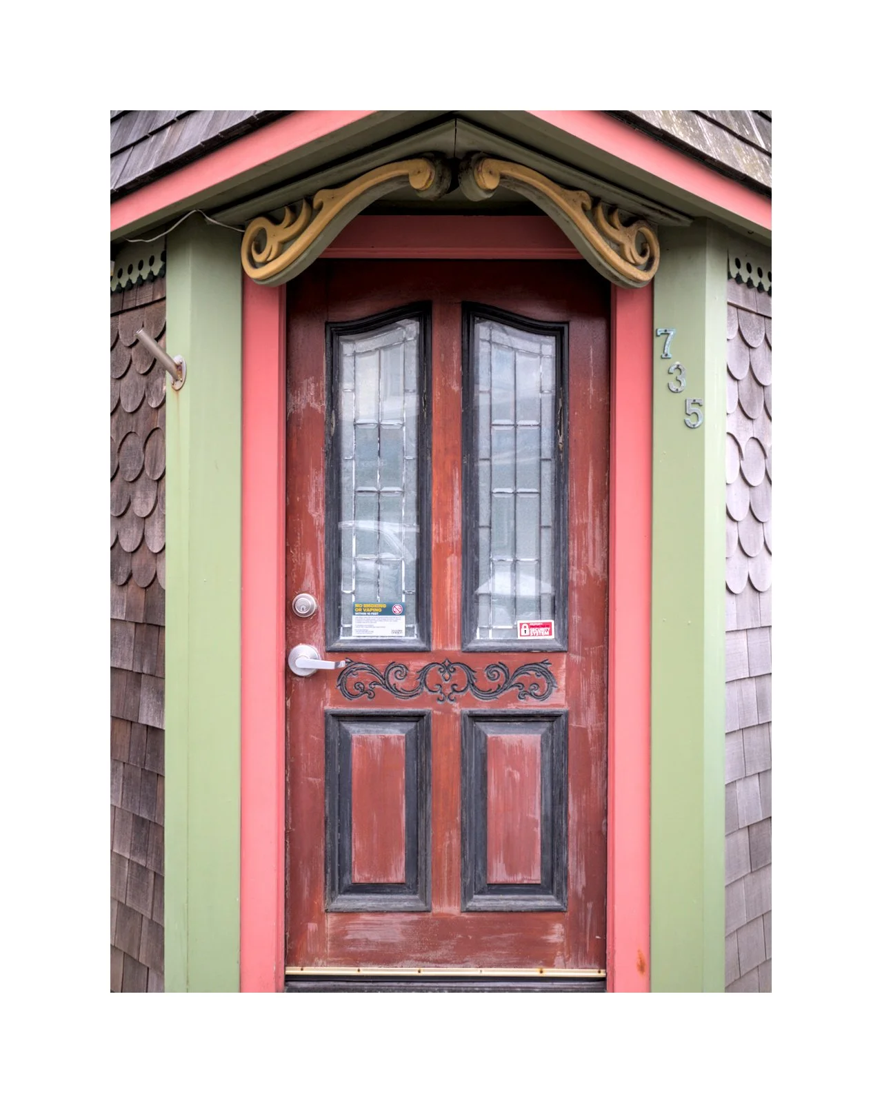 Front wooden door with decorative wrought iron accents, glass panels, and painted trim surrounded by shingle siding.