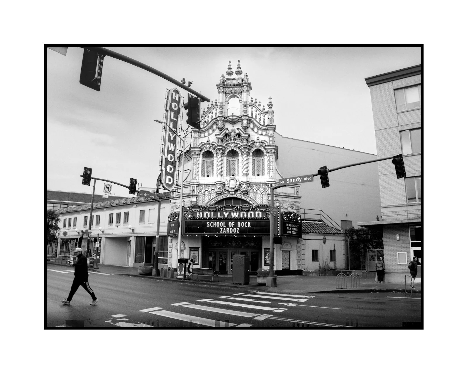Street view featuring the Hollywood Theatre with ornate architecture, a large signage, and a marquee advertising the School of Rock in Portland, Oregon, at the intersection of NE Sandy Blvd.