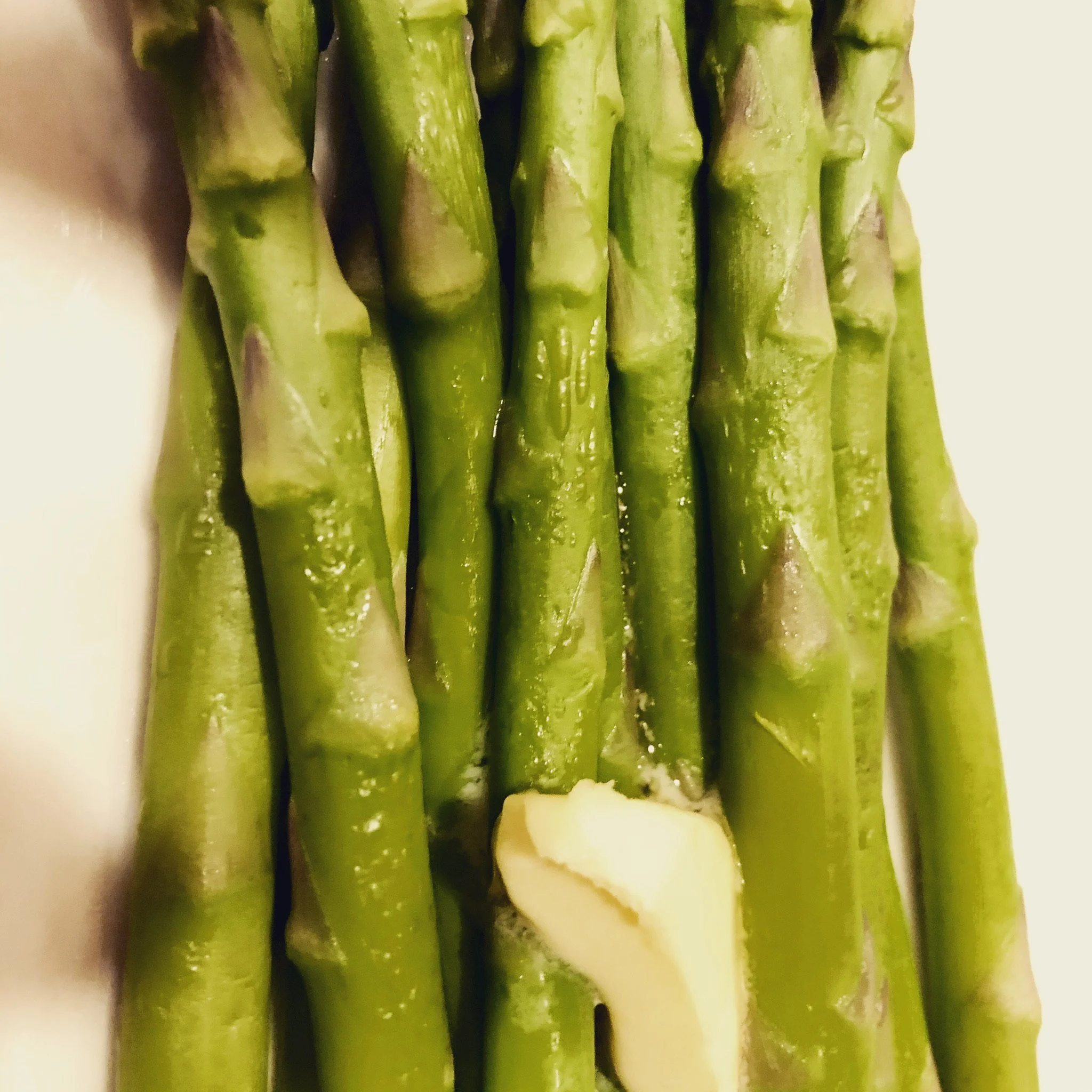 Close-up of fresh green asparagus spears with a peeled garlic clove at the bottom.