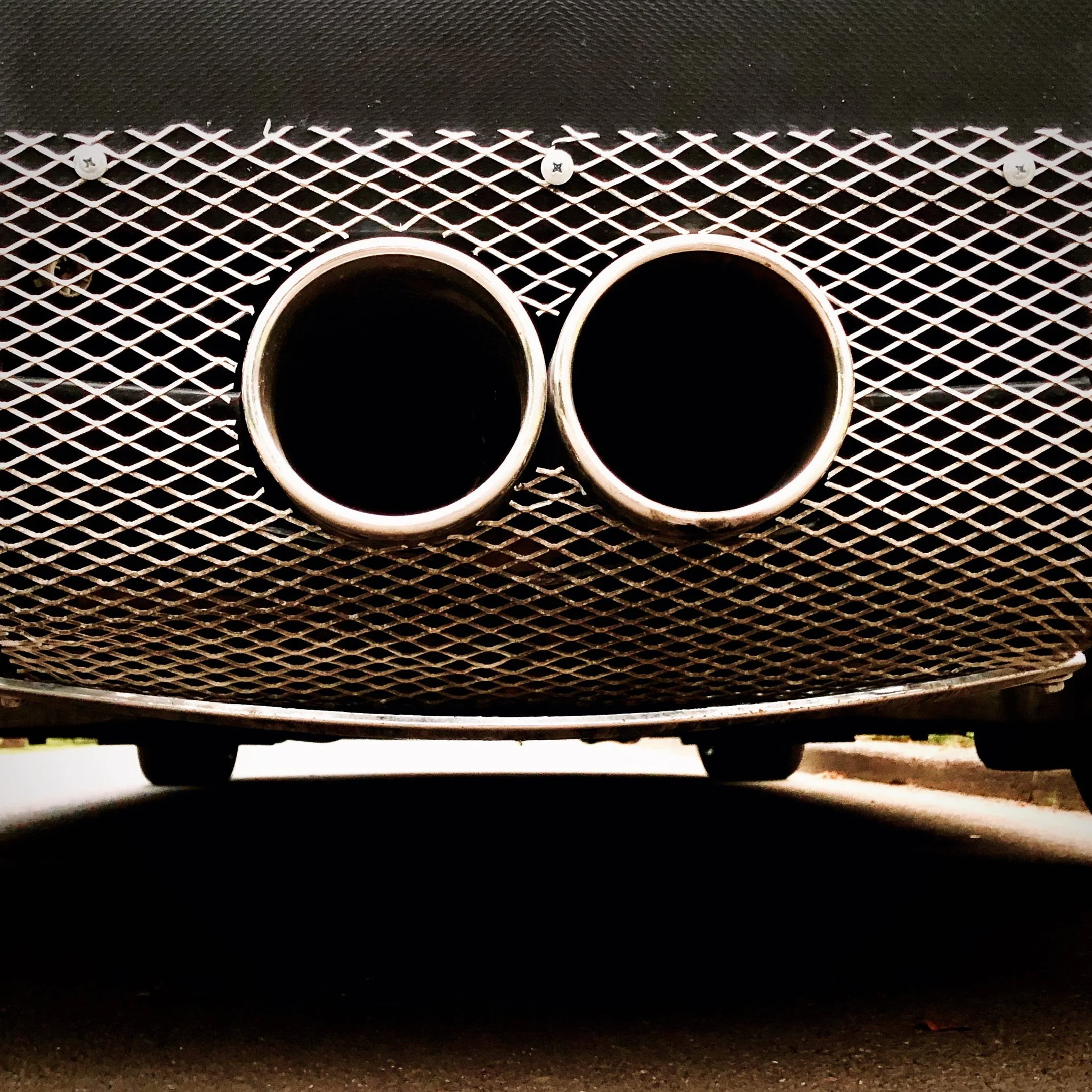 Close-up of a car's dual exhaust pipes beneath a mesh grille.