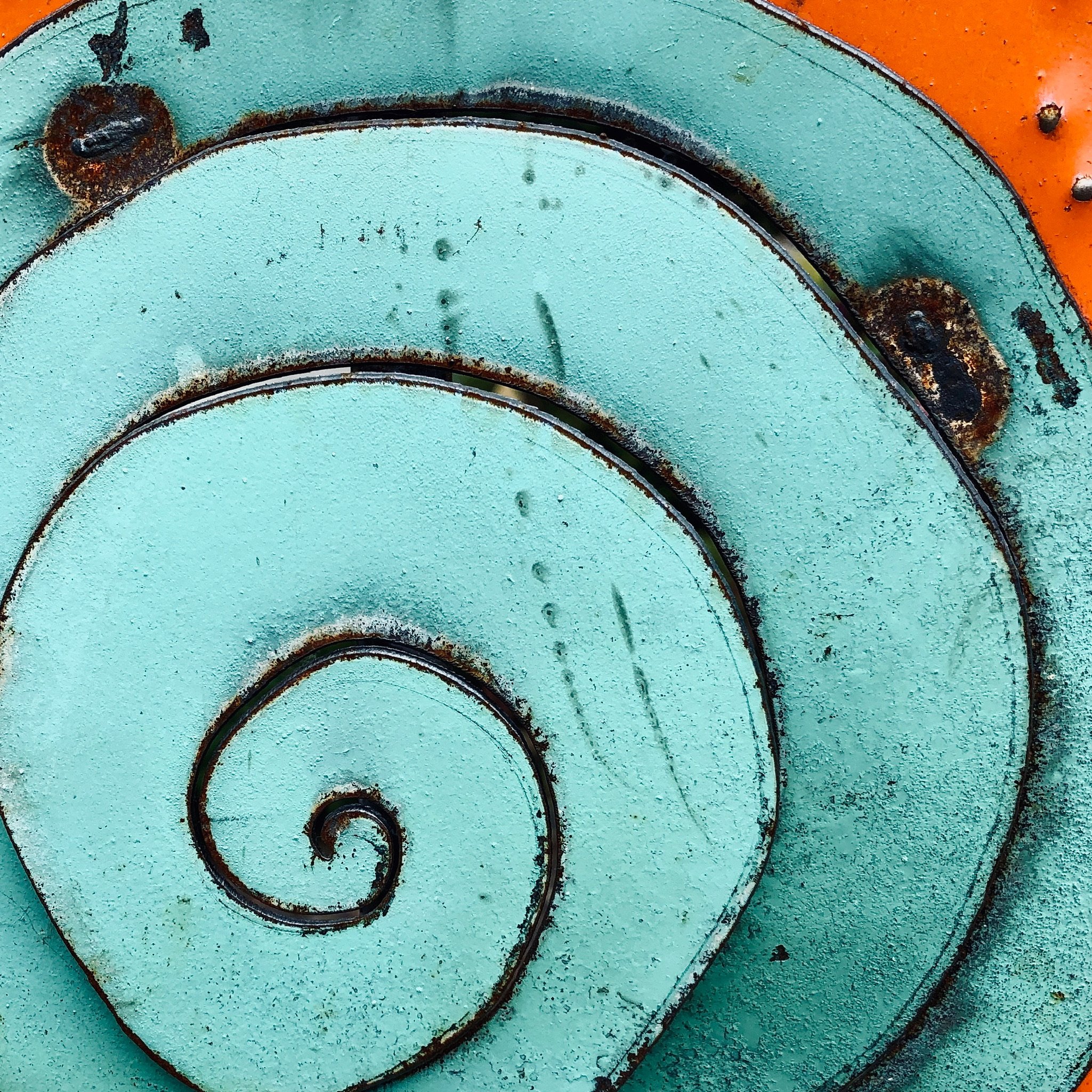 Close-up of turquoise and orange spiraled metal surface with rust and weathering details.