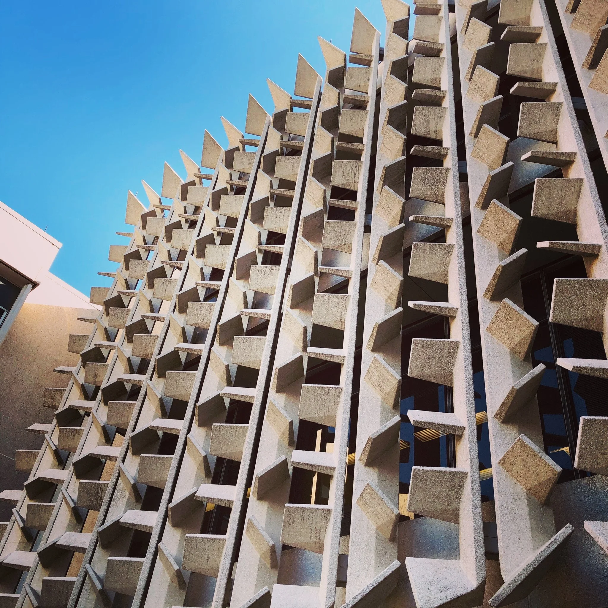 Close-up view of a modern building's facade with a geometric pattern of protruding concrete blocks and vertical elements against a clear blue sky.
