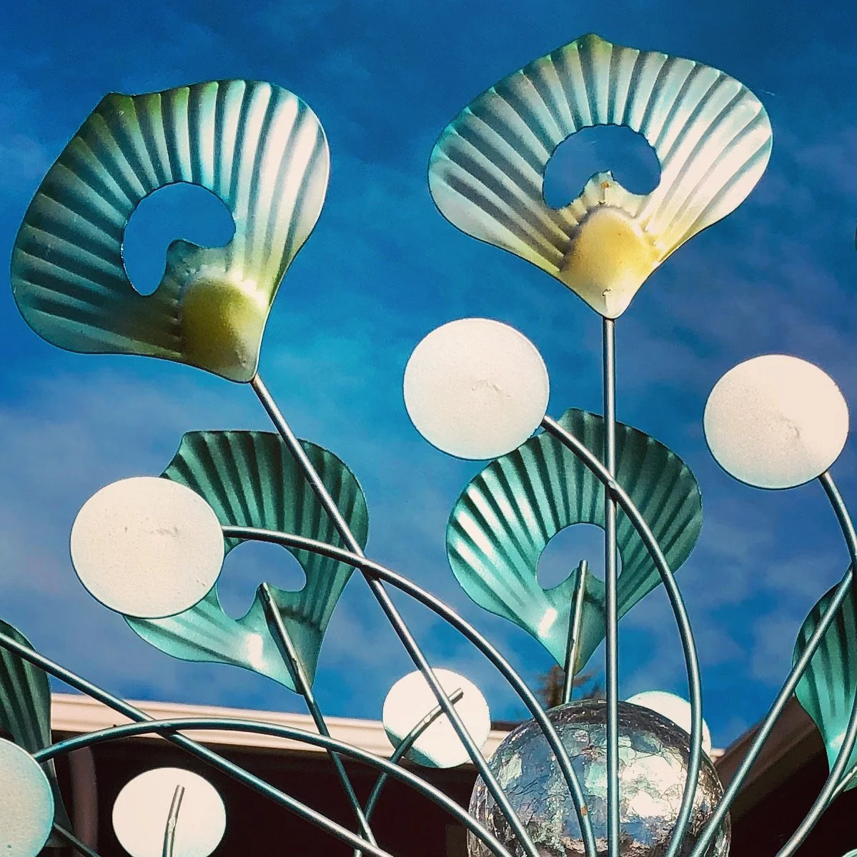 Decorative metal sculpture resembling sea shells with white spherical lights and a globe at the bottom, set against a blue sky.