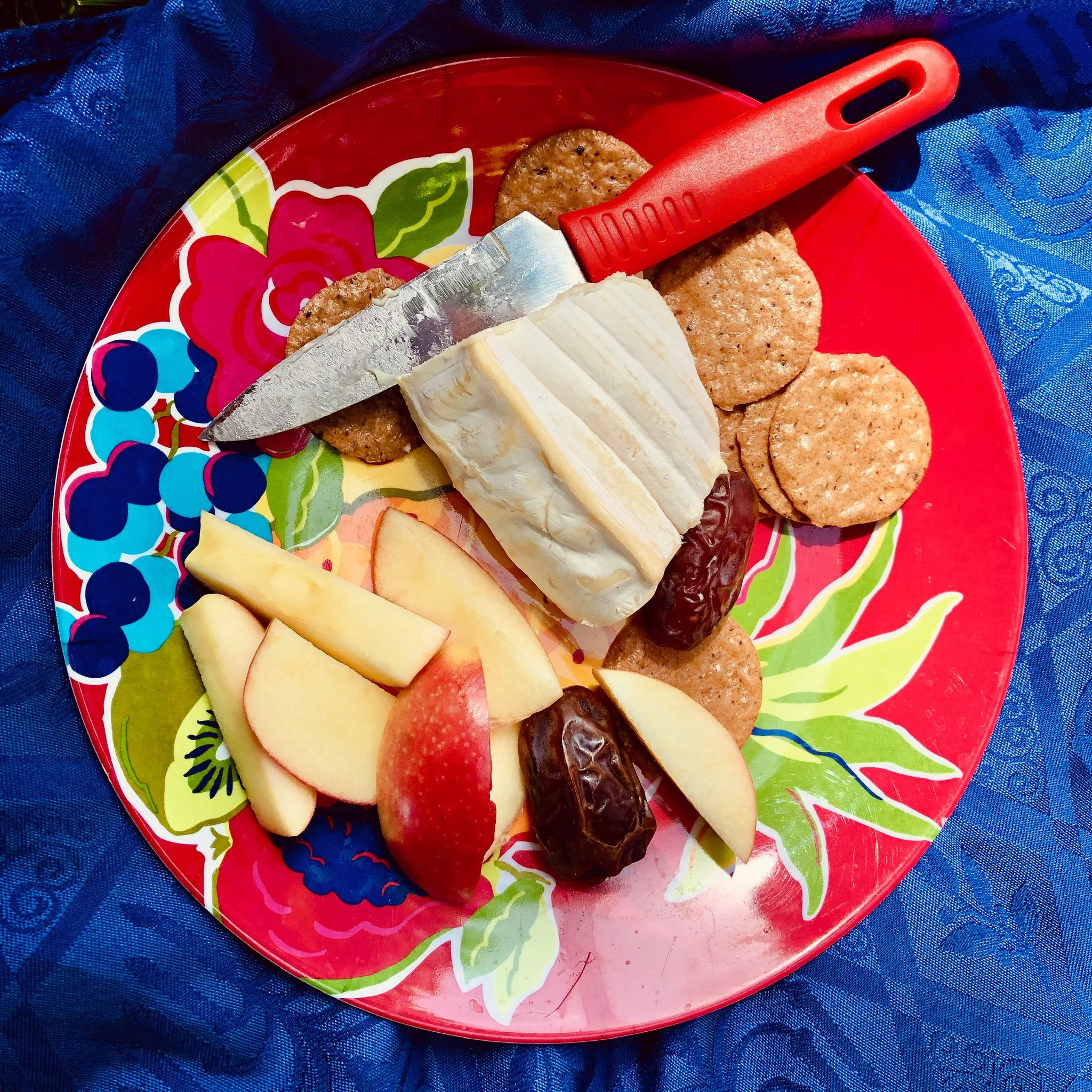 A colorful plate with cheese, apple slices, graham crackers, dates, and a knife.