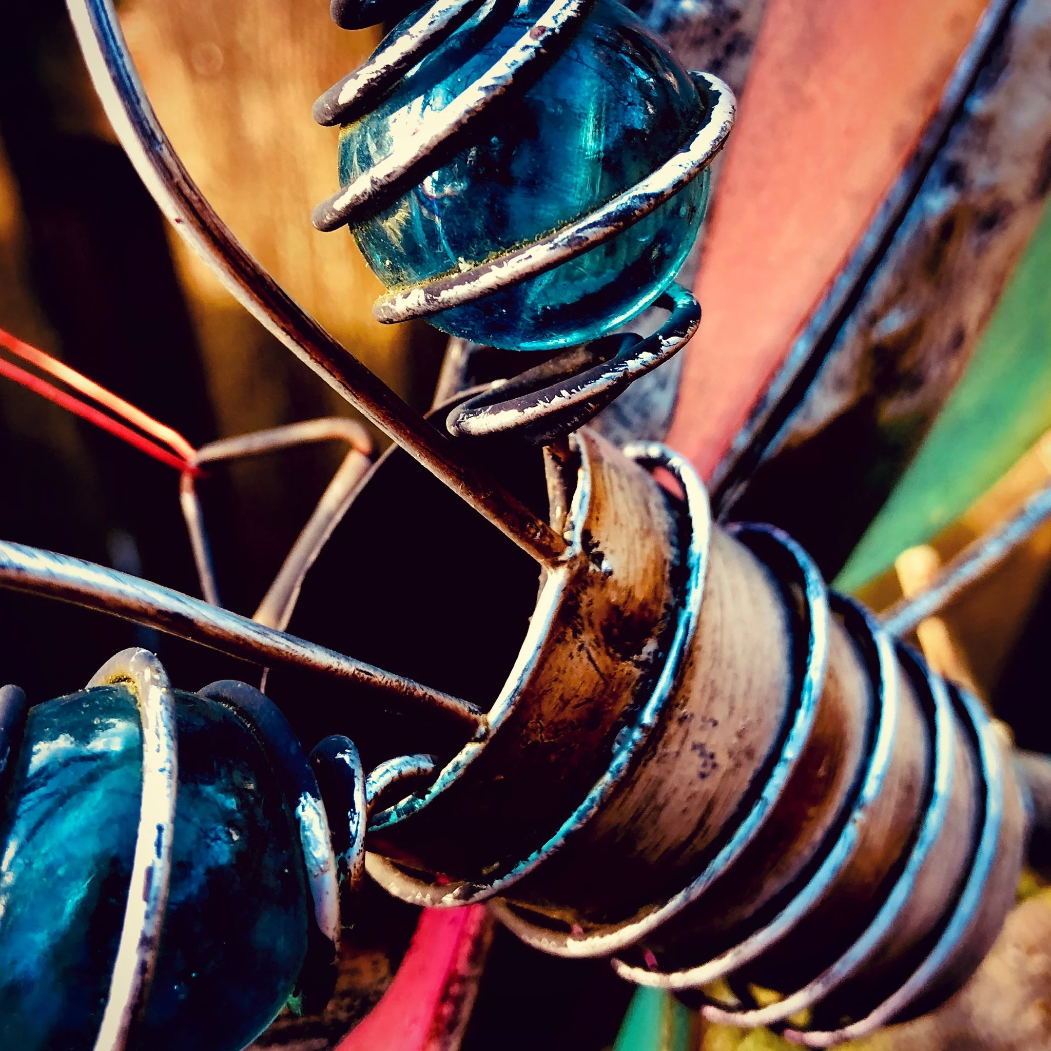 Close-up of a decorative glass sculpture with a blue glass orb wrapped in metal coils, mounted on a metal structure with colorful background elements.