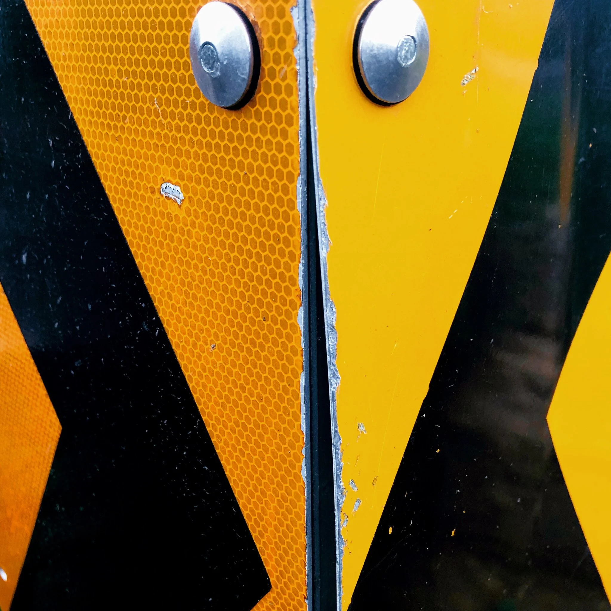 Close-up view of a traffic or safety barrier with reflective yellow and black striped pattern, showing hardware and some paint chipping.