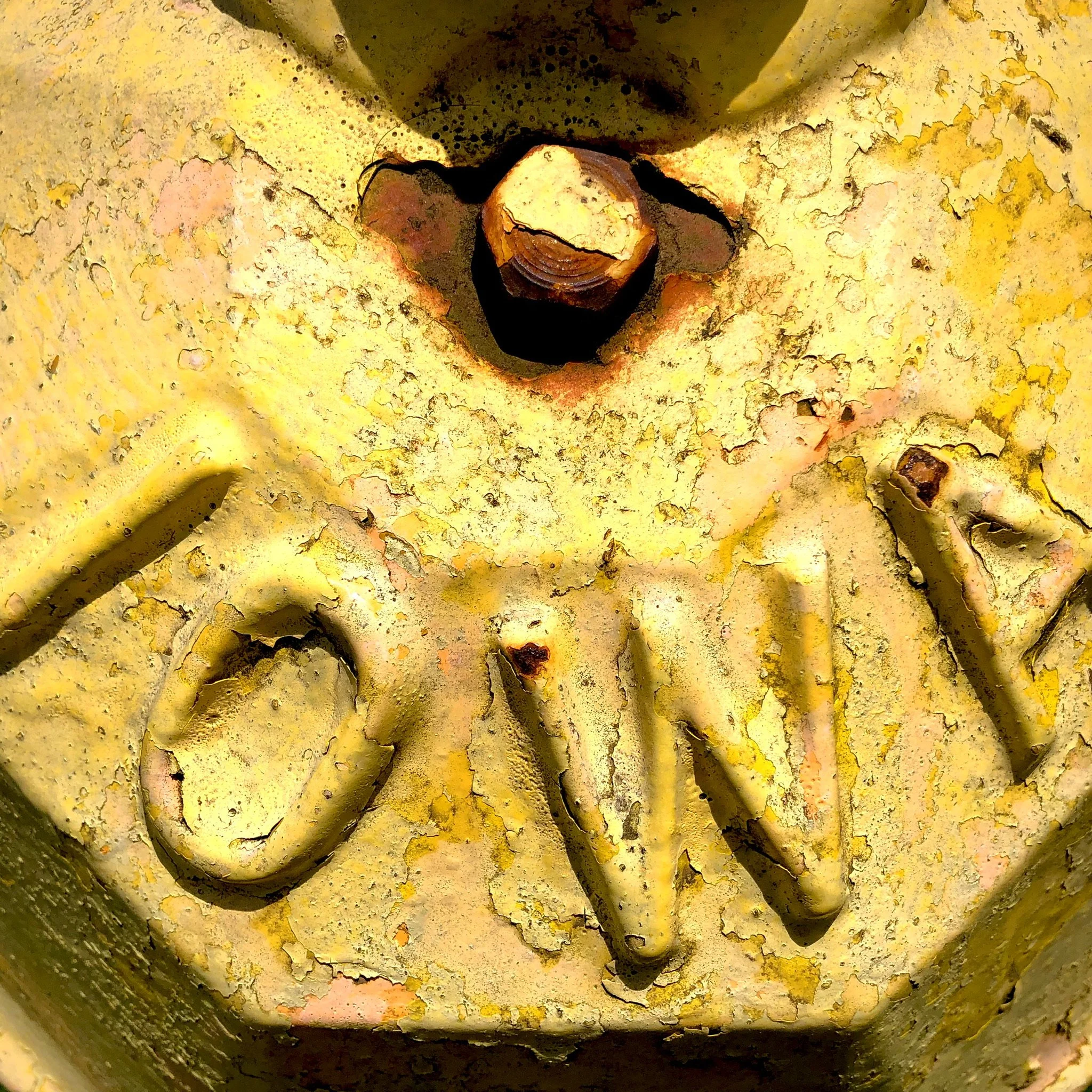 Close-up of a yellow painted metal surface with the raised letters spelling 'ON' and a rusted bolt hole.